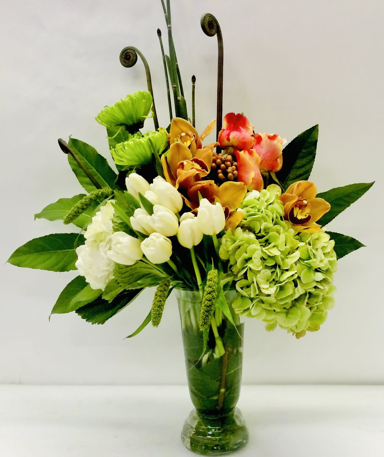 Mixed floral arrangement in a glass vase with green hydrangea and orchids