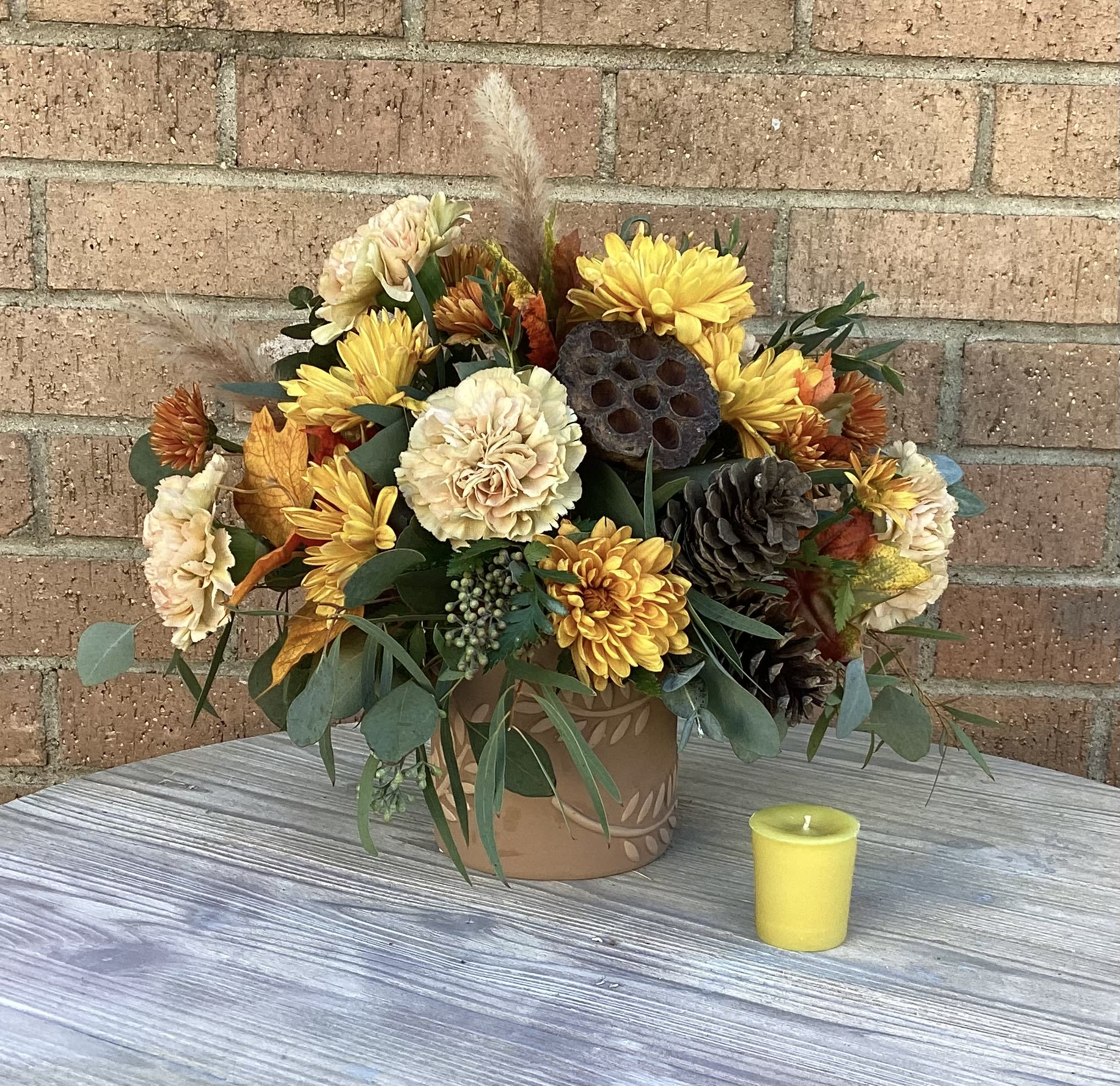 Autumn flower arrangement in a decorative pot with a small yellow candle nearby