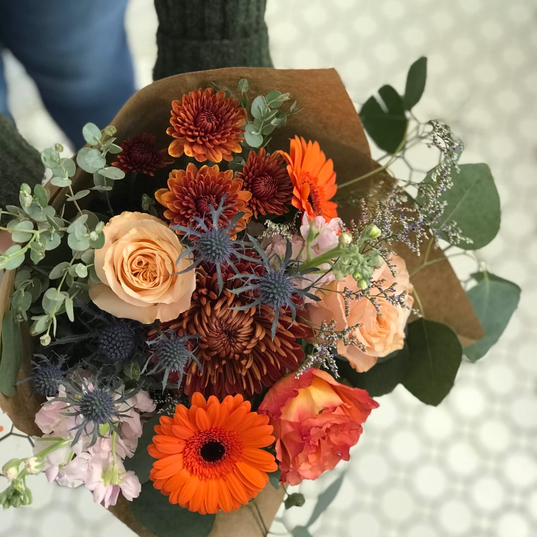 Bouquet of orange and peach flowers with blue thistle in brown paper