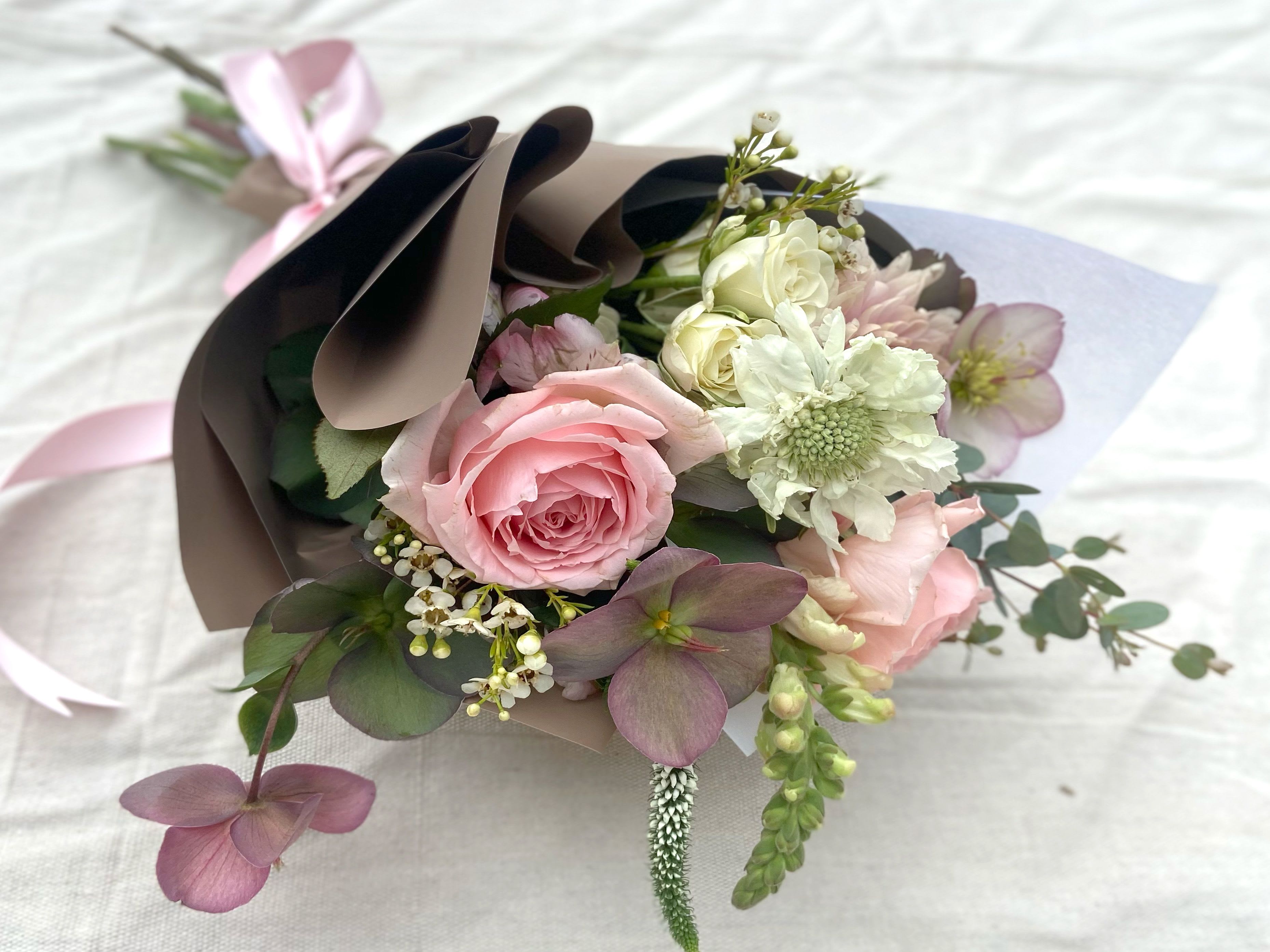 Pink and white bouquet wrapped in brown paper with a ribbon