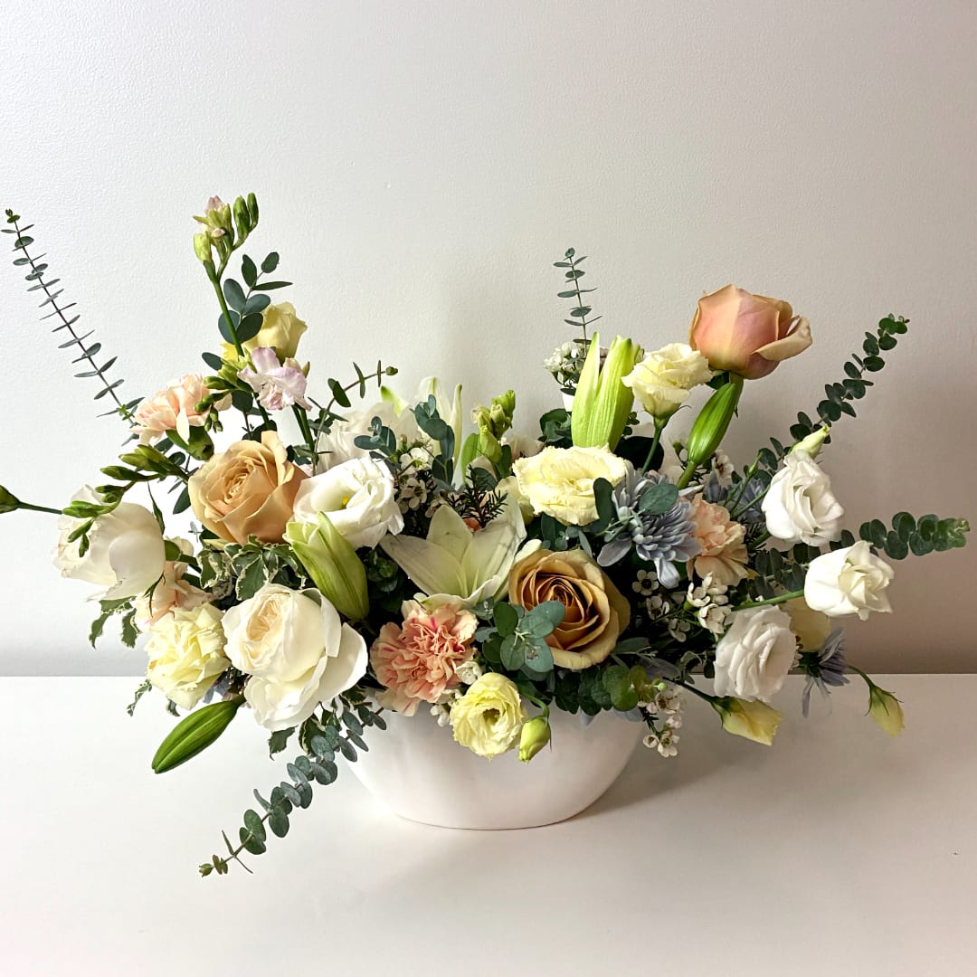 Mixed bouquet of roses, lilies, and carnations in a white bowl vase
