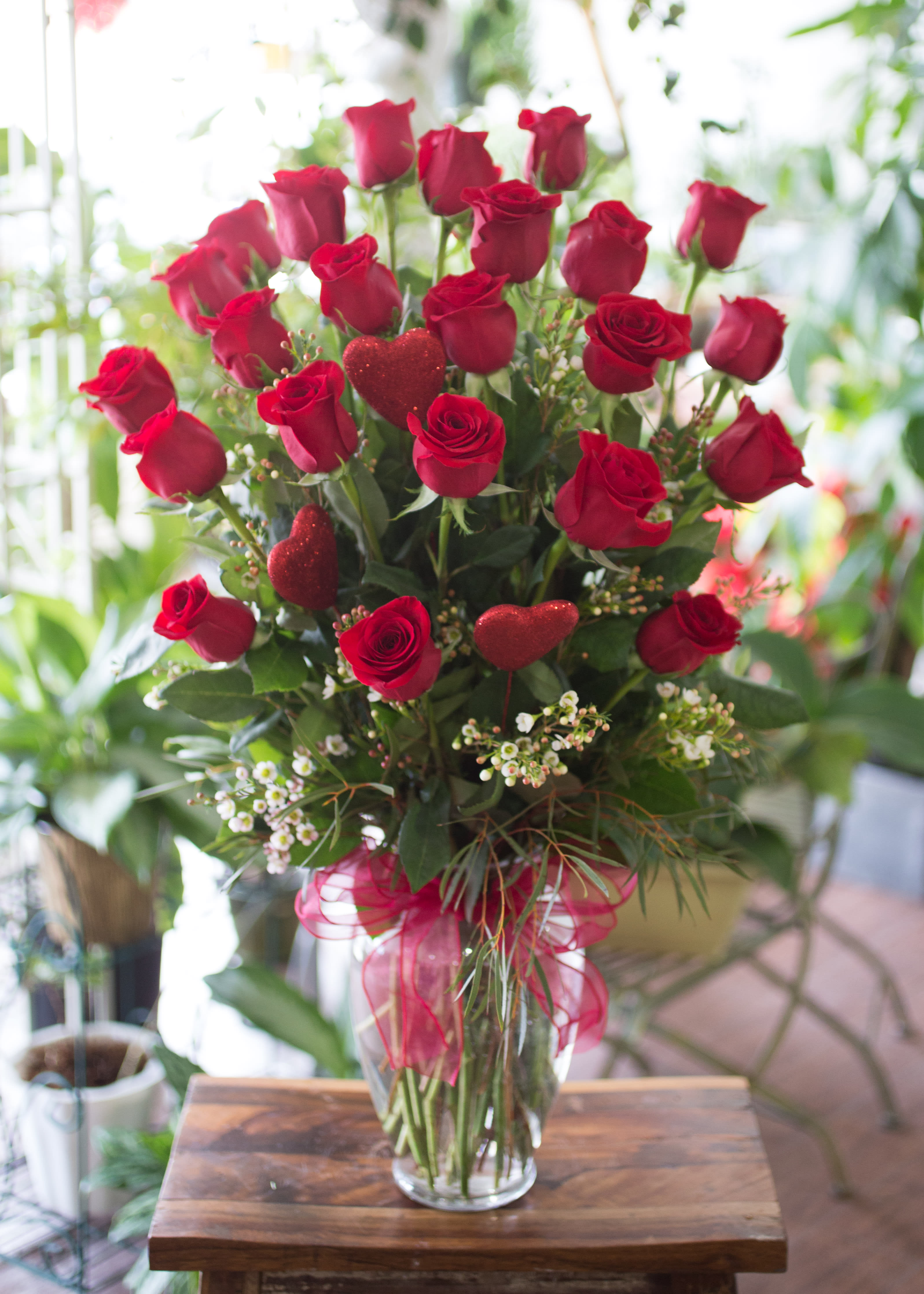 Red roses in a clear glass vase with glittery heart picks