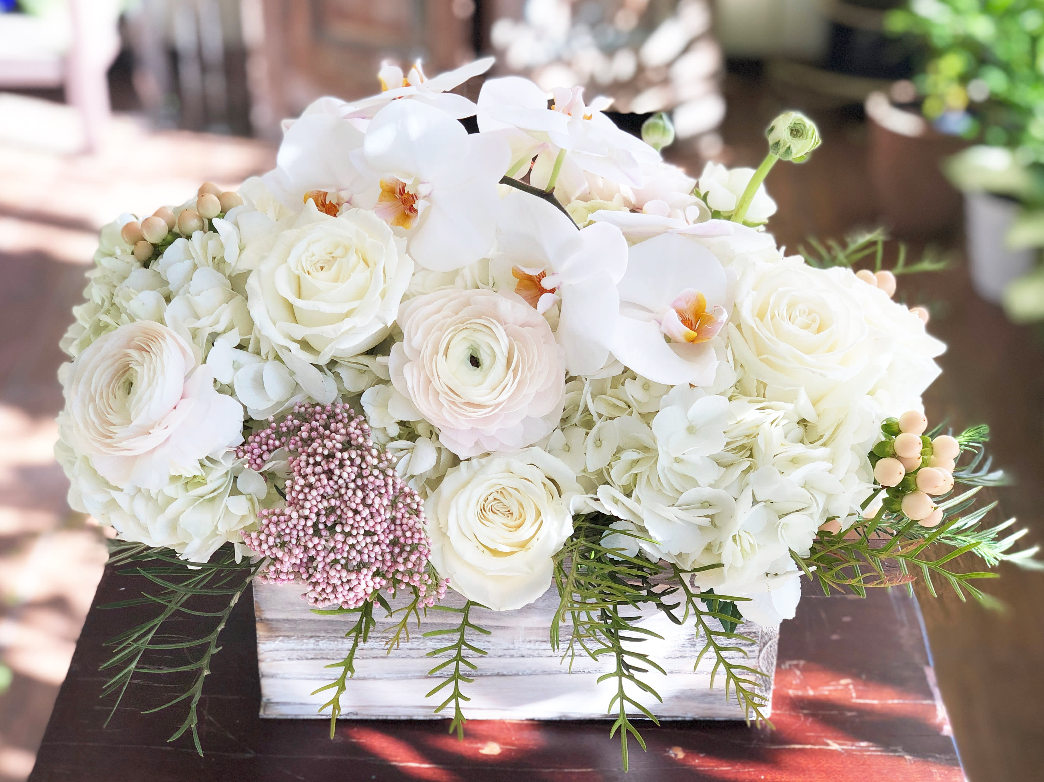 White floral arrangement in a rectangular wooden box with orchids and roses