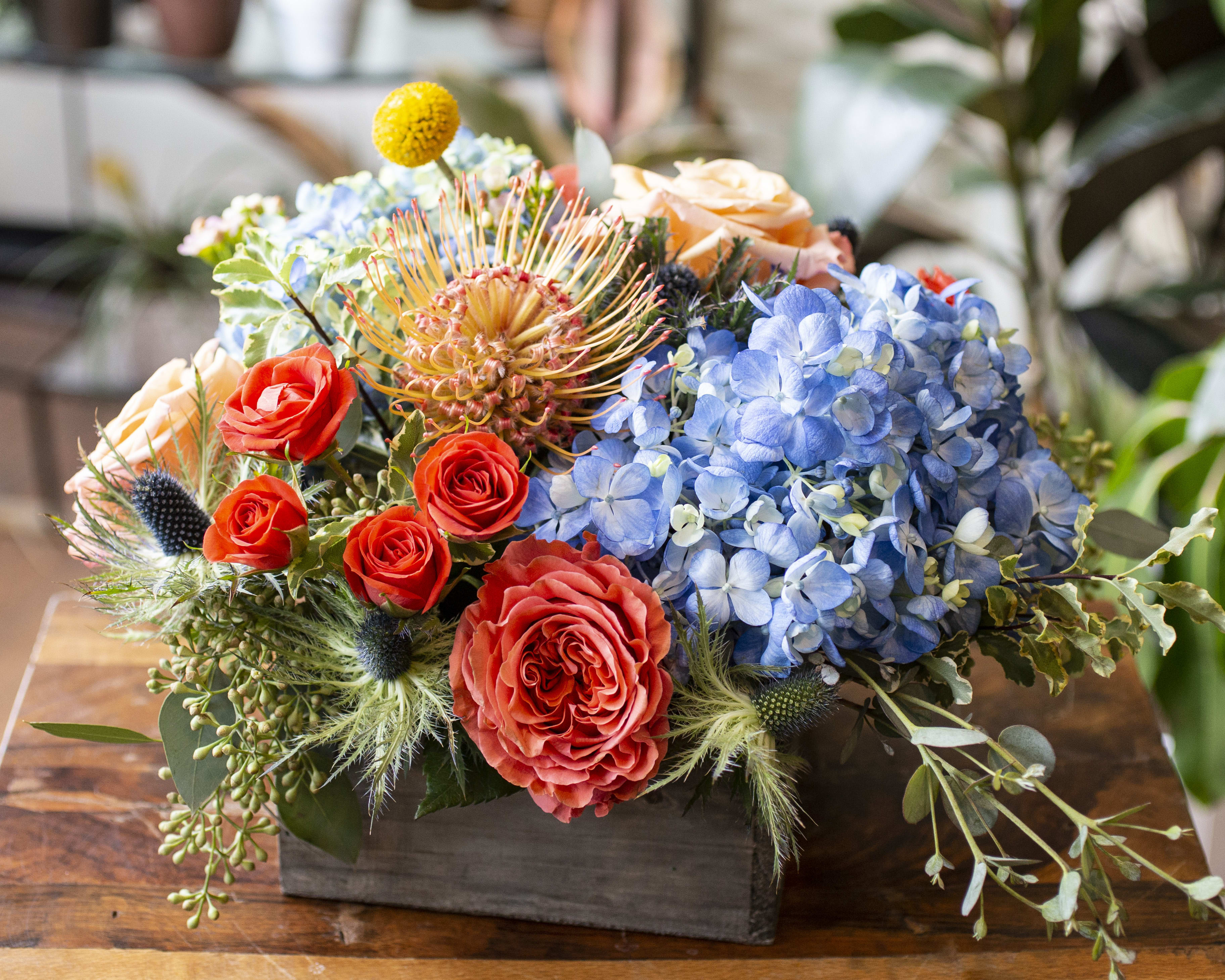 Colorful floral arrangement in a dark wooden box with roses and blue hydrangeas