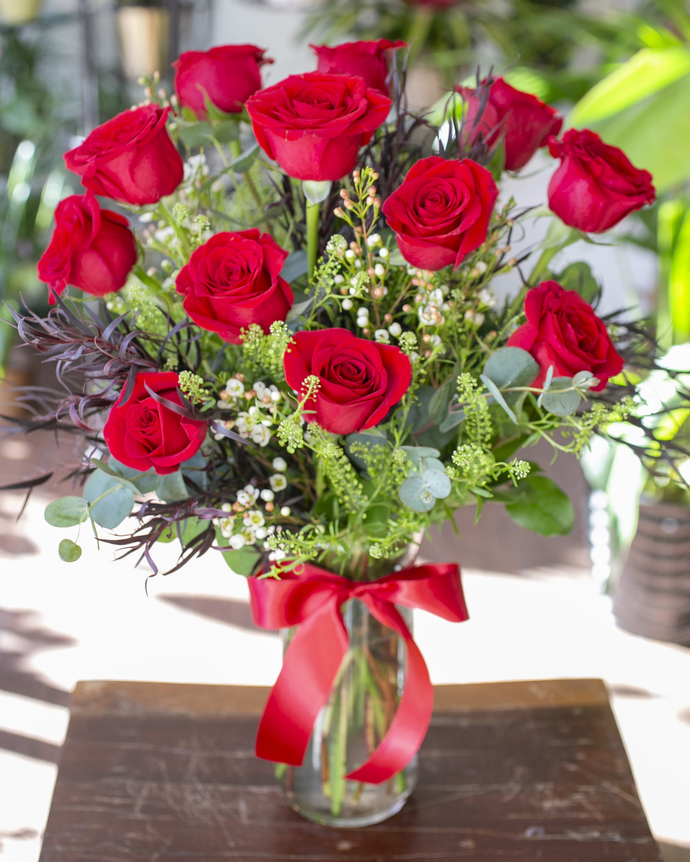 Red roses arranged in a glass vase with a red ribbon
