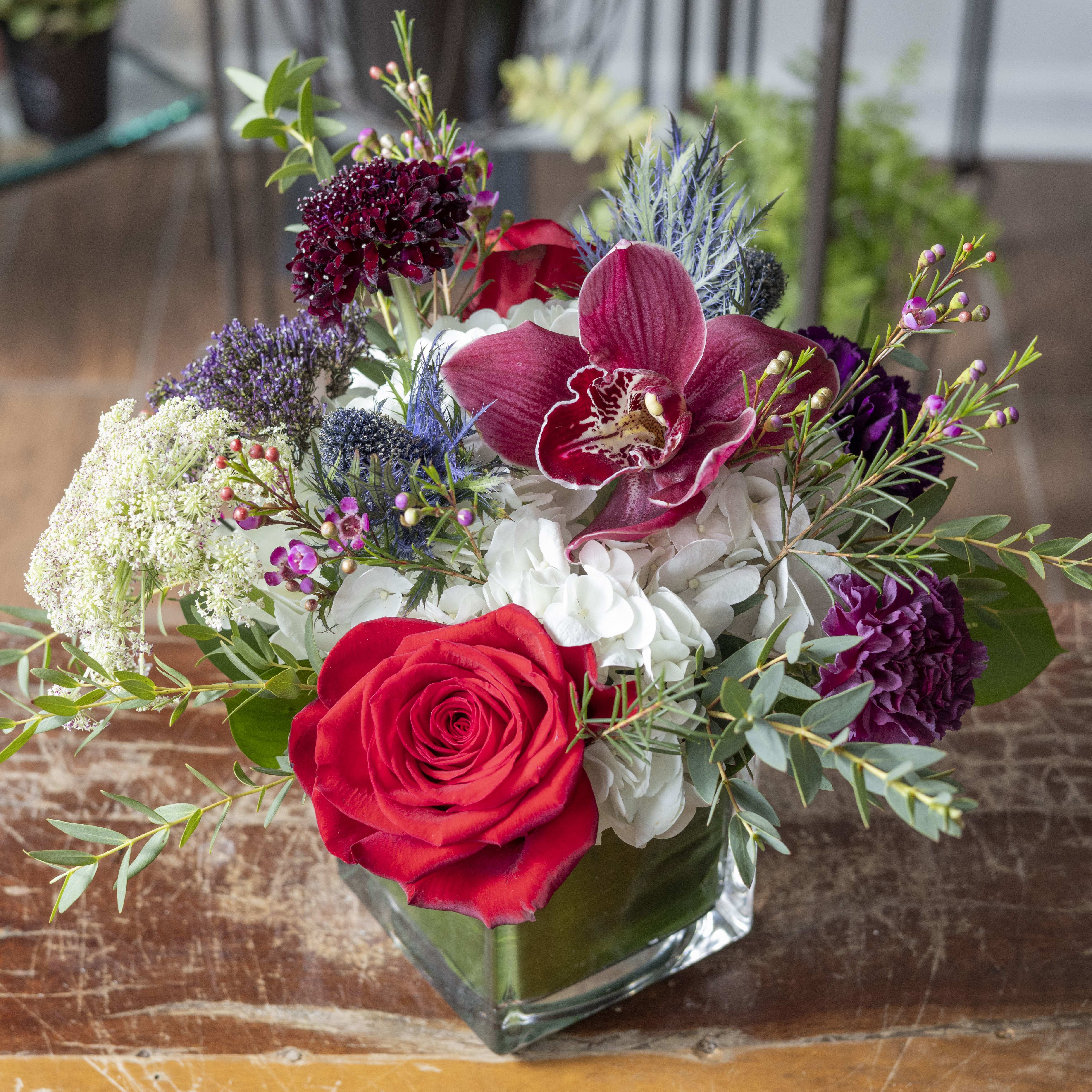 Bouquet of red roses, orchids, and white hydrangeas in a glass vase