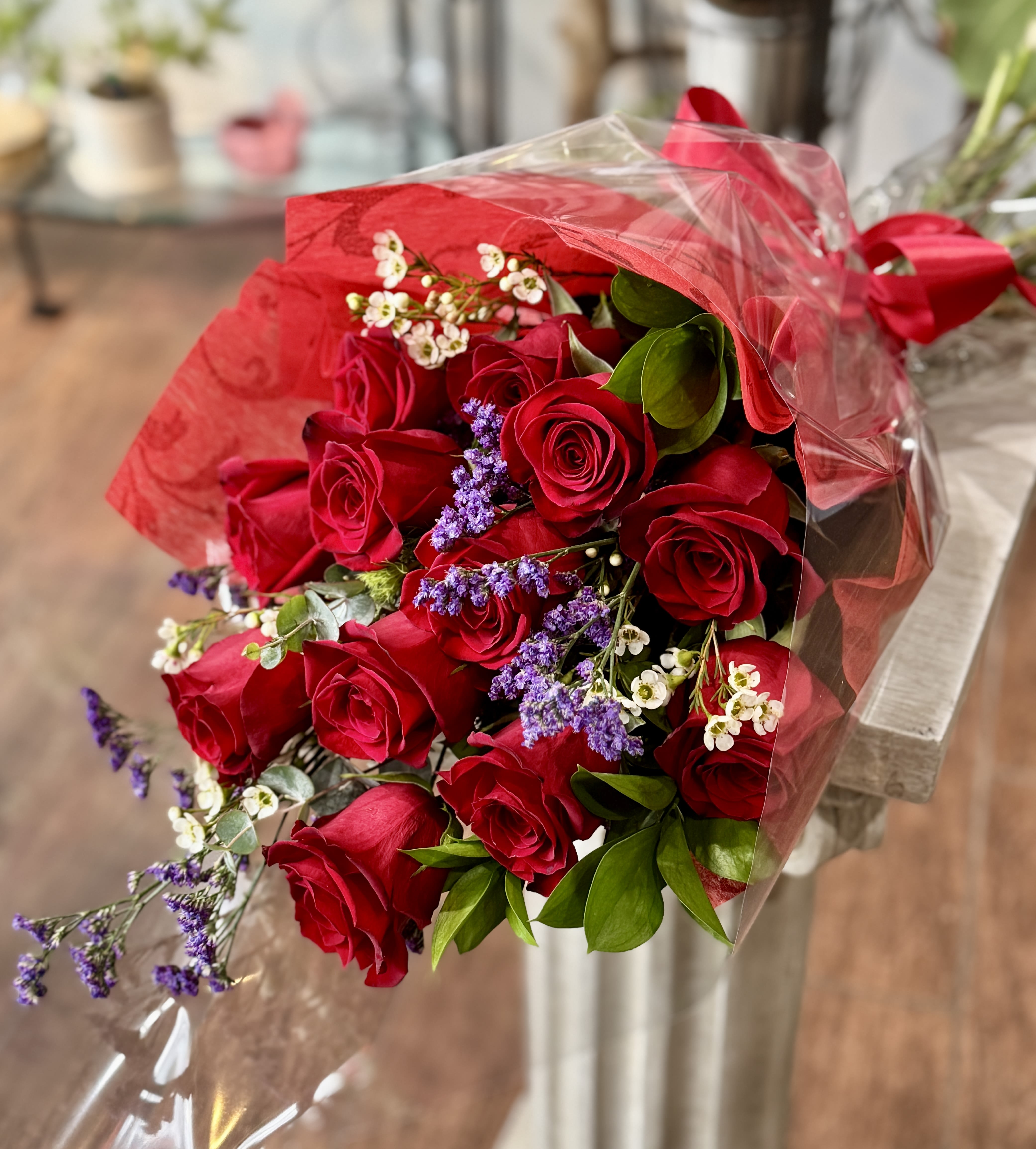 Bouquet of red roses with purple filler flowers wrapped in red and clear plastic