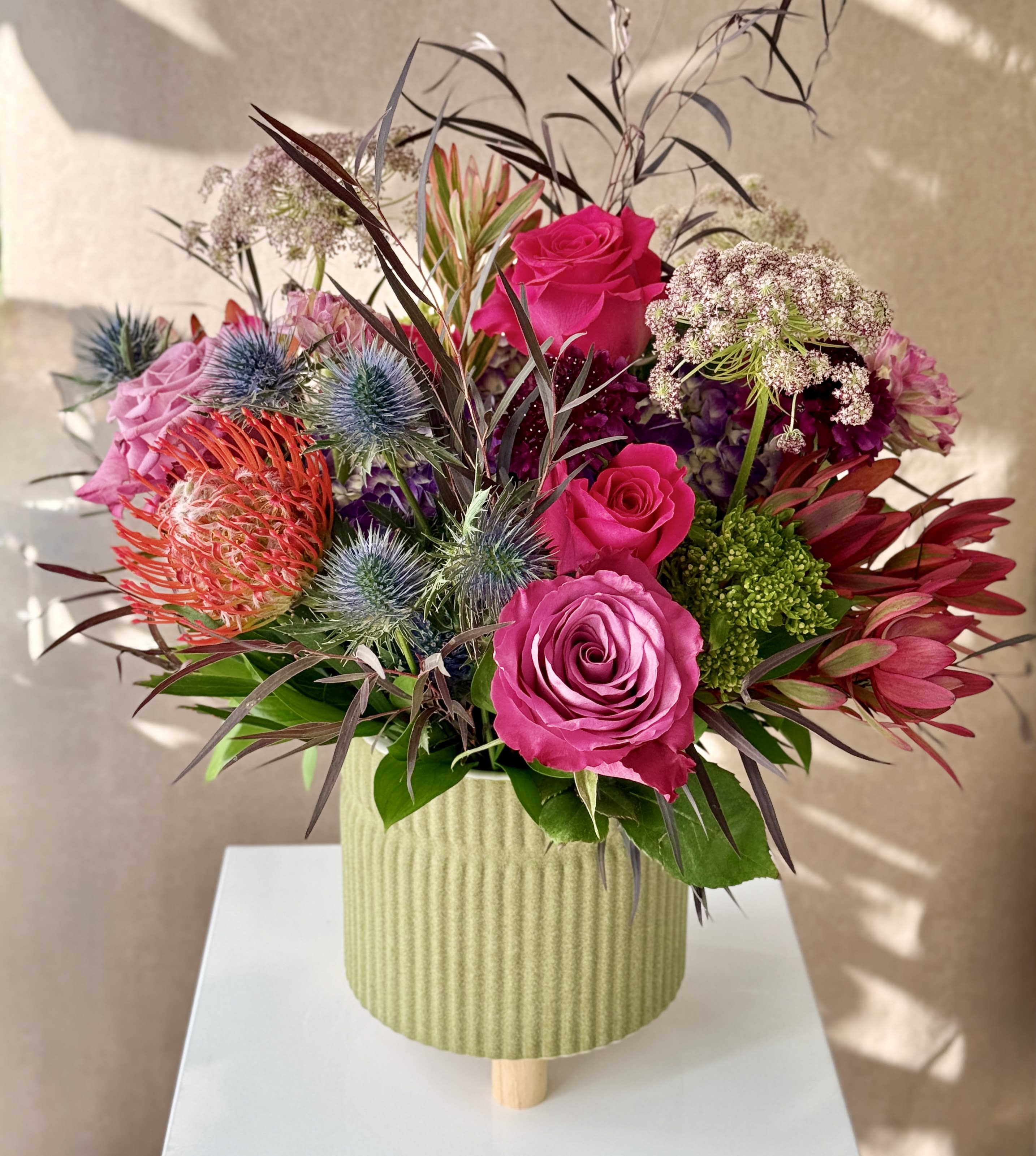 Bouquet of pink roses and spiky flowers in a ribbed green vase