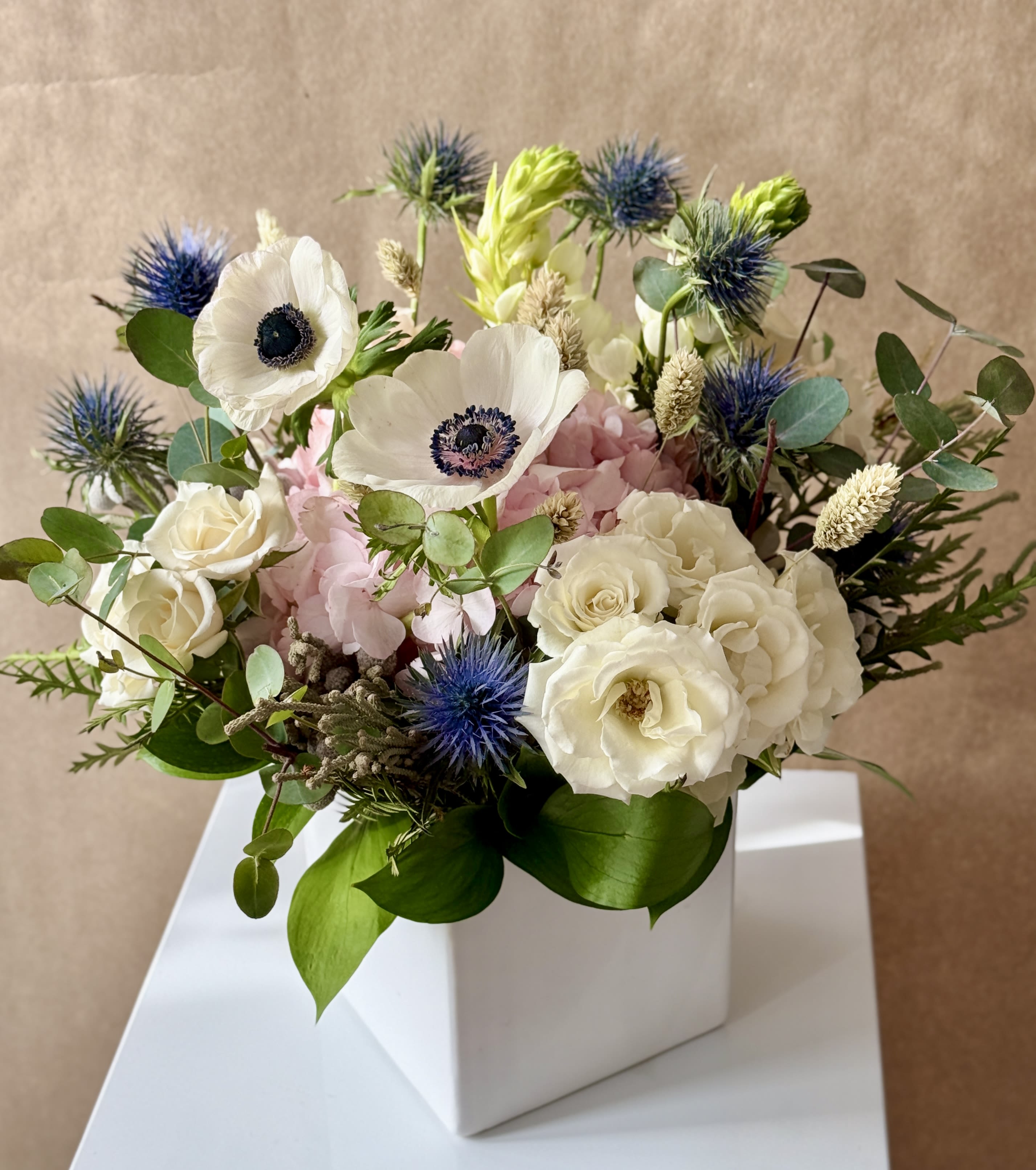 White and pink floral arrangement in a white box with blue thistle-like blooms