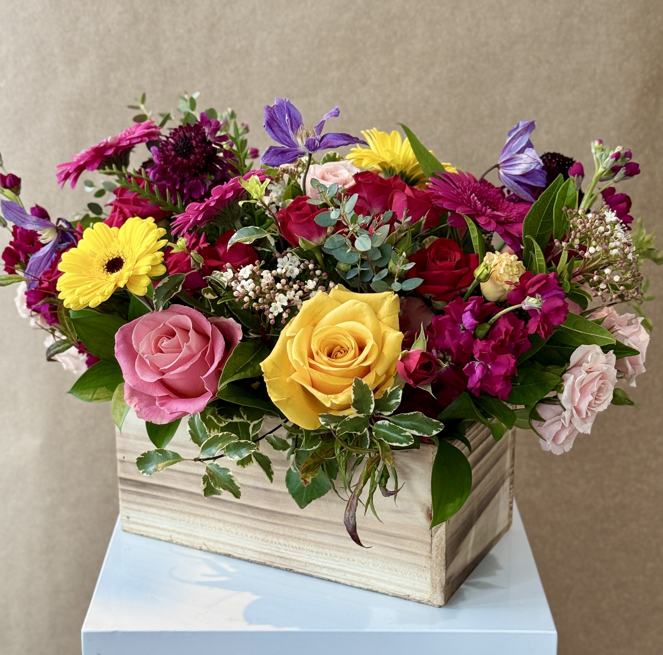 Mixed bouquet of roses, gerbera daisies, and purple blooms in a wooden box
