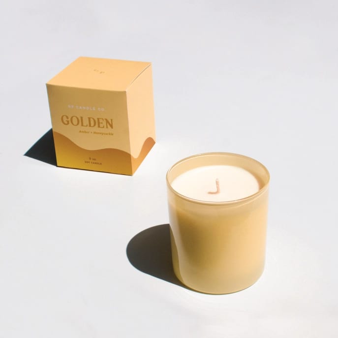 Gold candle in a glass jar beside its box
