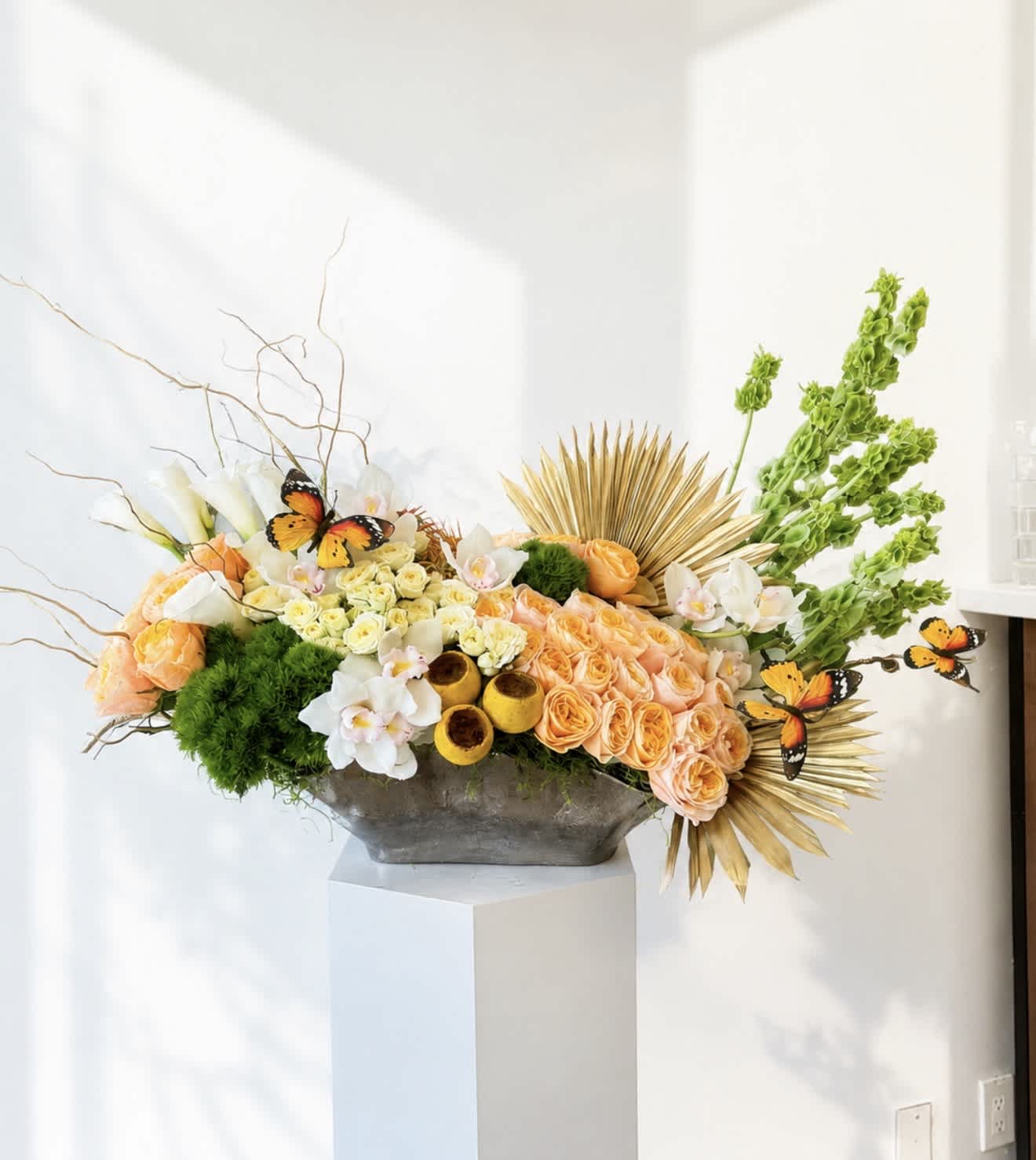 Large floral arrangement with peach roses, white orchids, and green accents in a gray vase