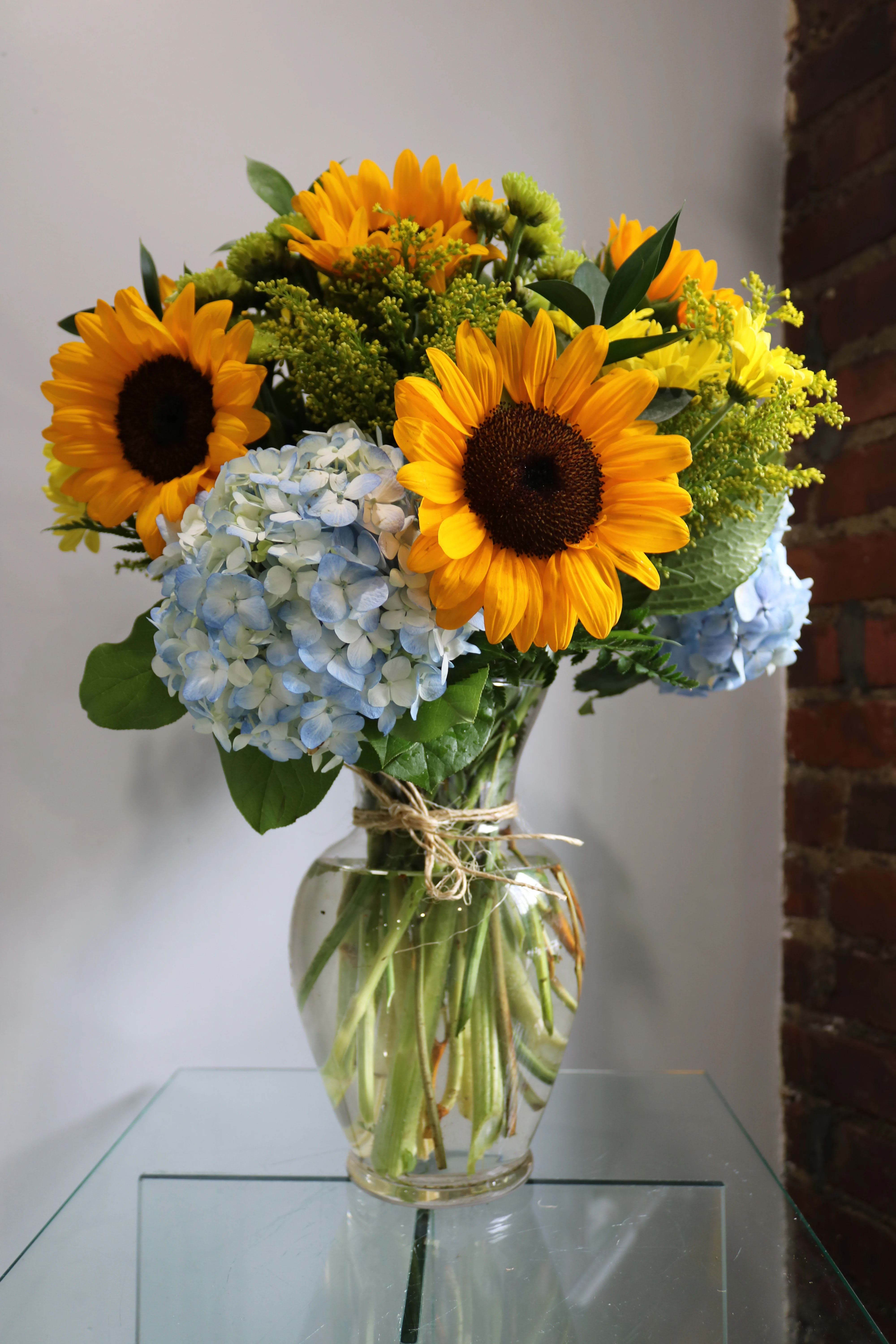 Sunflowers and blue hydrangeas arranged in a glass vase