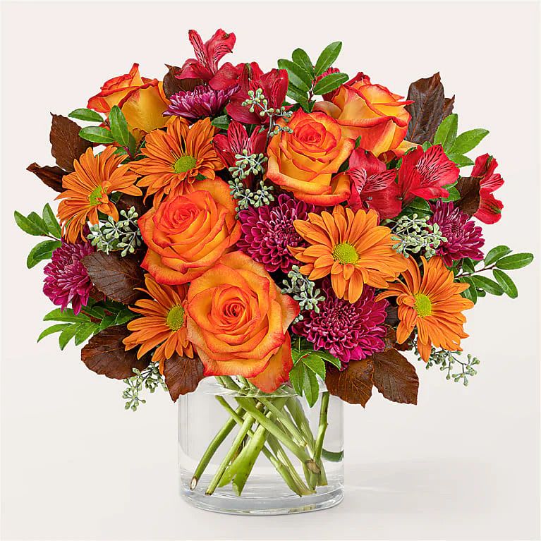 Orange roses and purple mums in a clear glass vase