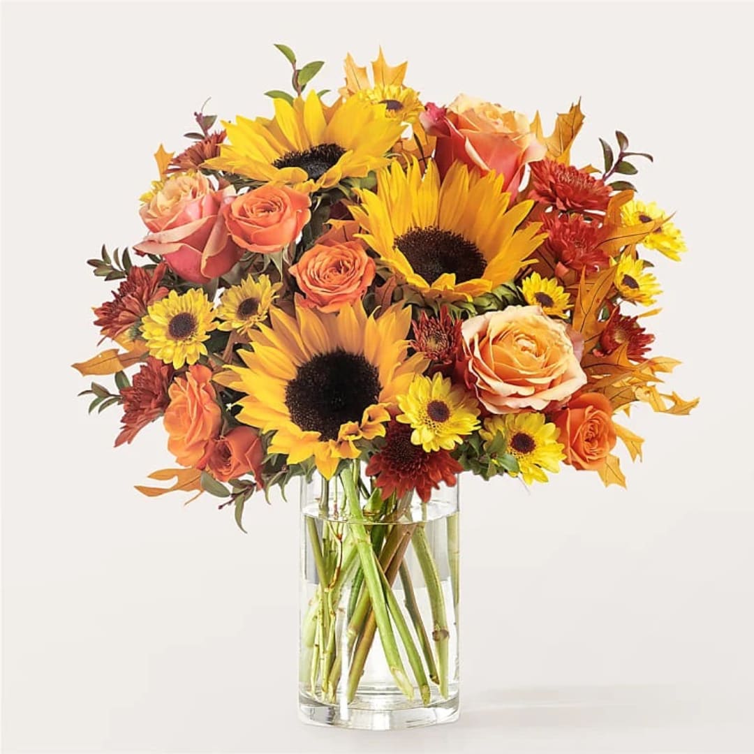 Bouquet of sunflowers, roses, and mums in a clear glass vase
