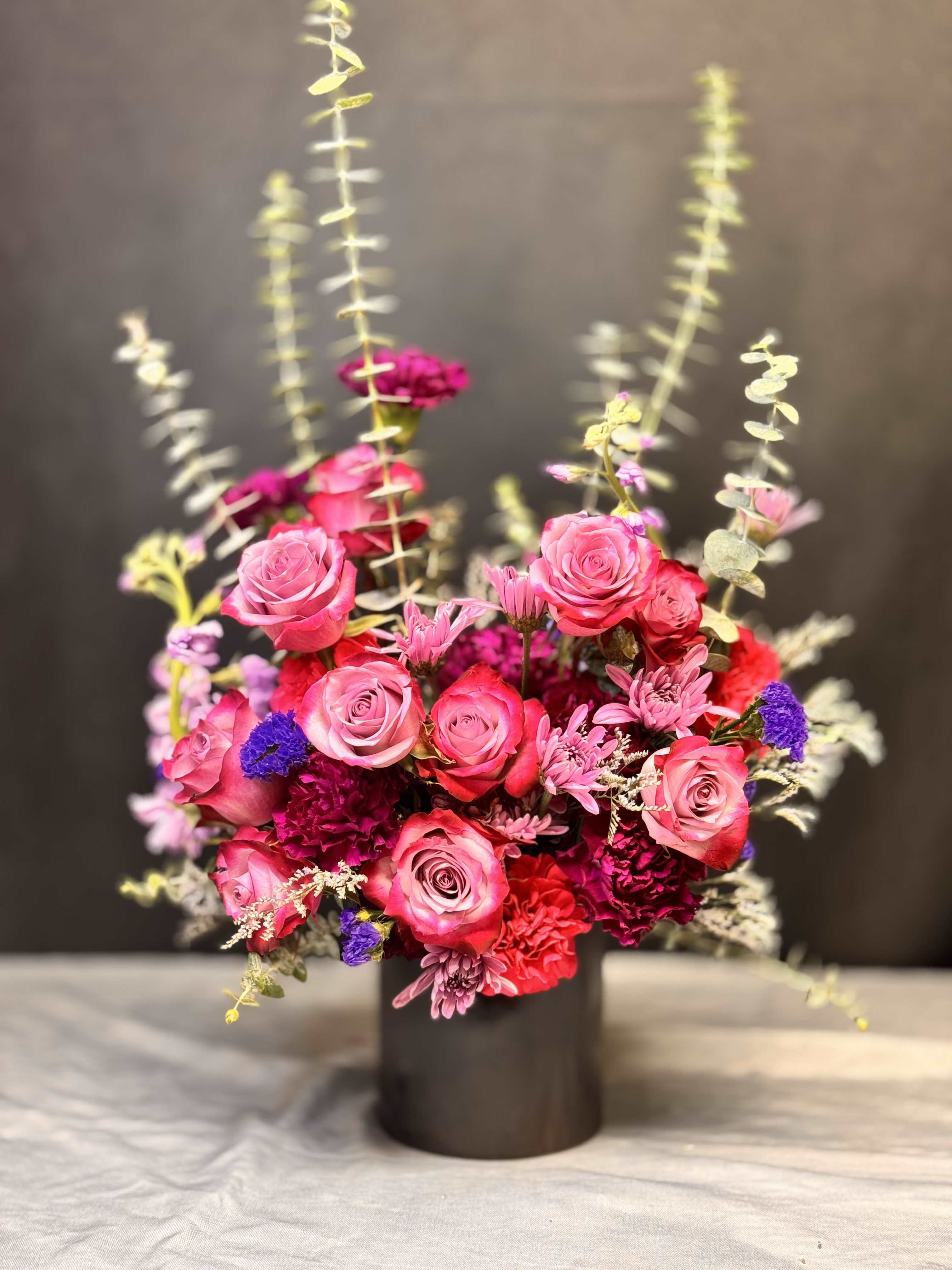 Vibrant arrangement of pink roses and red carnations with purple accents in a black cylinder vase
