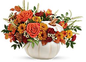 Orange and red floral arrangement in a white pumpkin vase