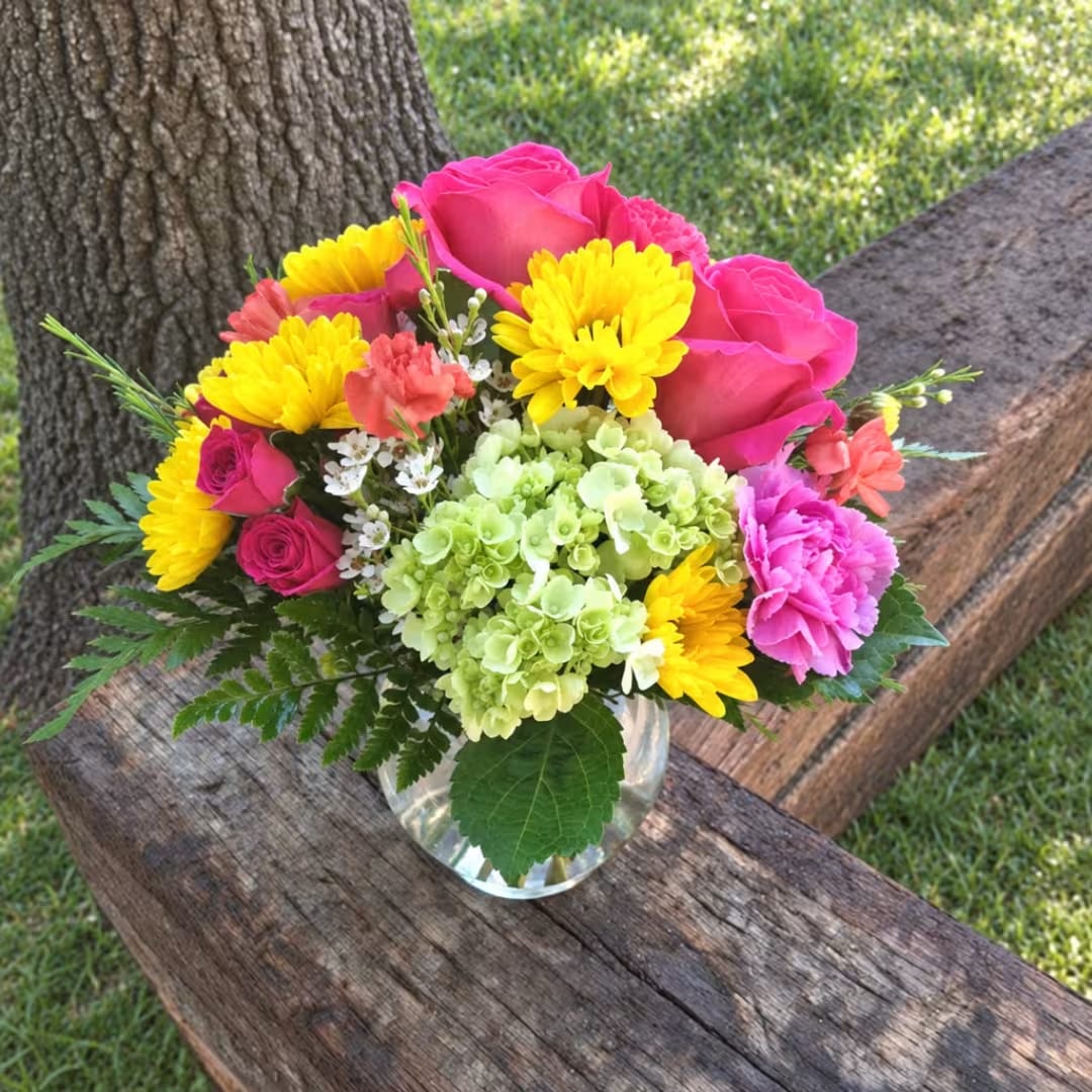 Colorful bouquet of pink roses, yellow mums, and green hydrangea in a glass vase