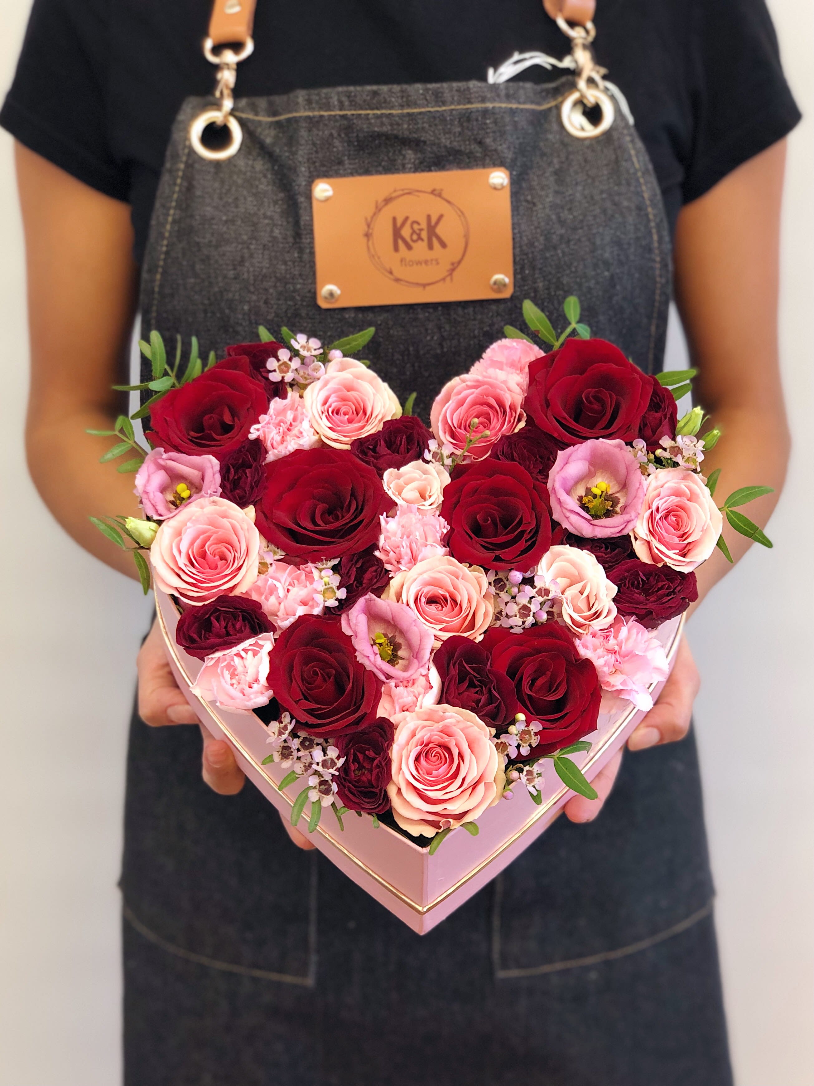 Heart-shaped box of red and pink roses held by a person