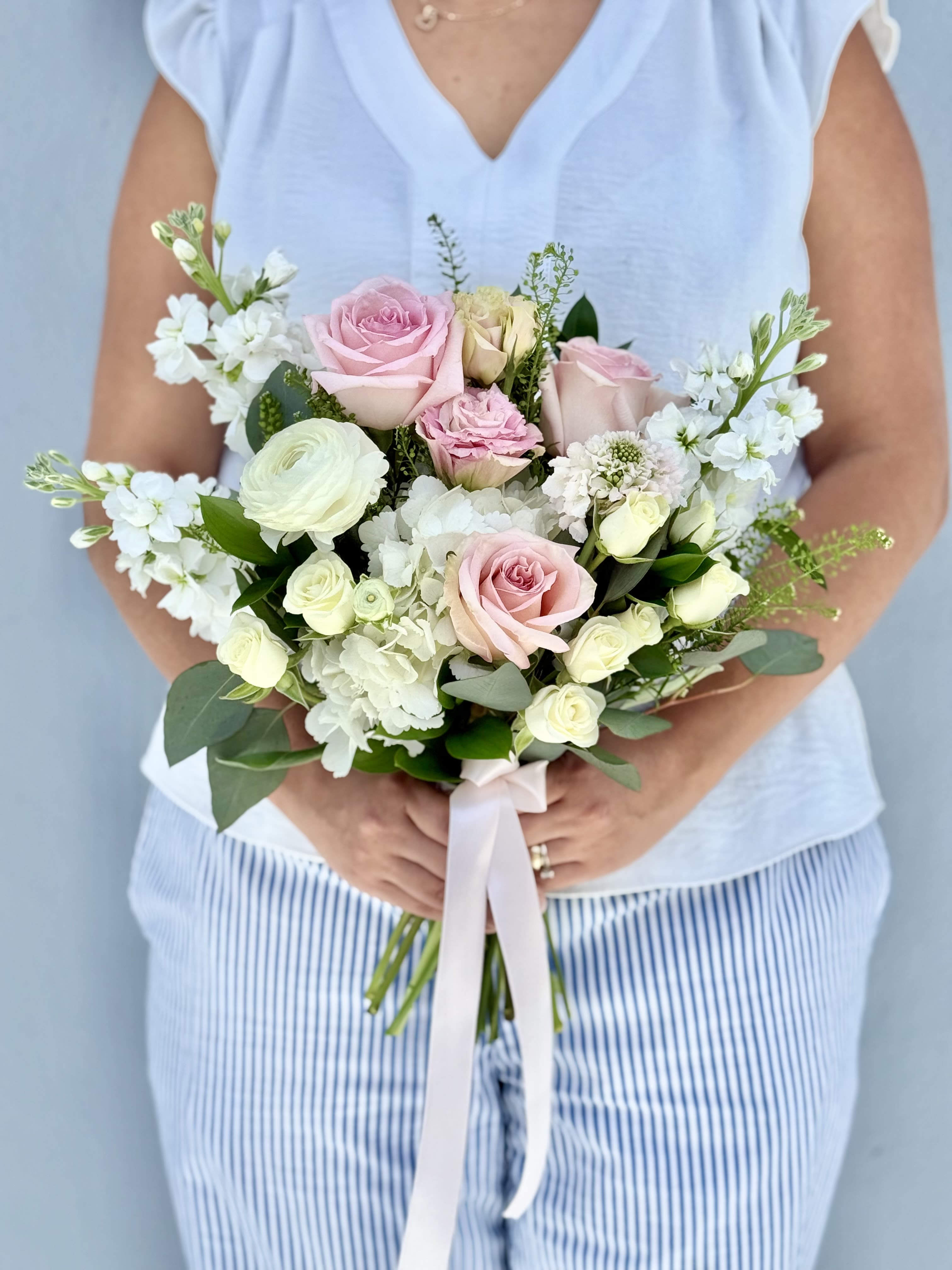 Handheld bouquet of pink and white roses with white blooms and ribbon