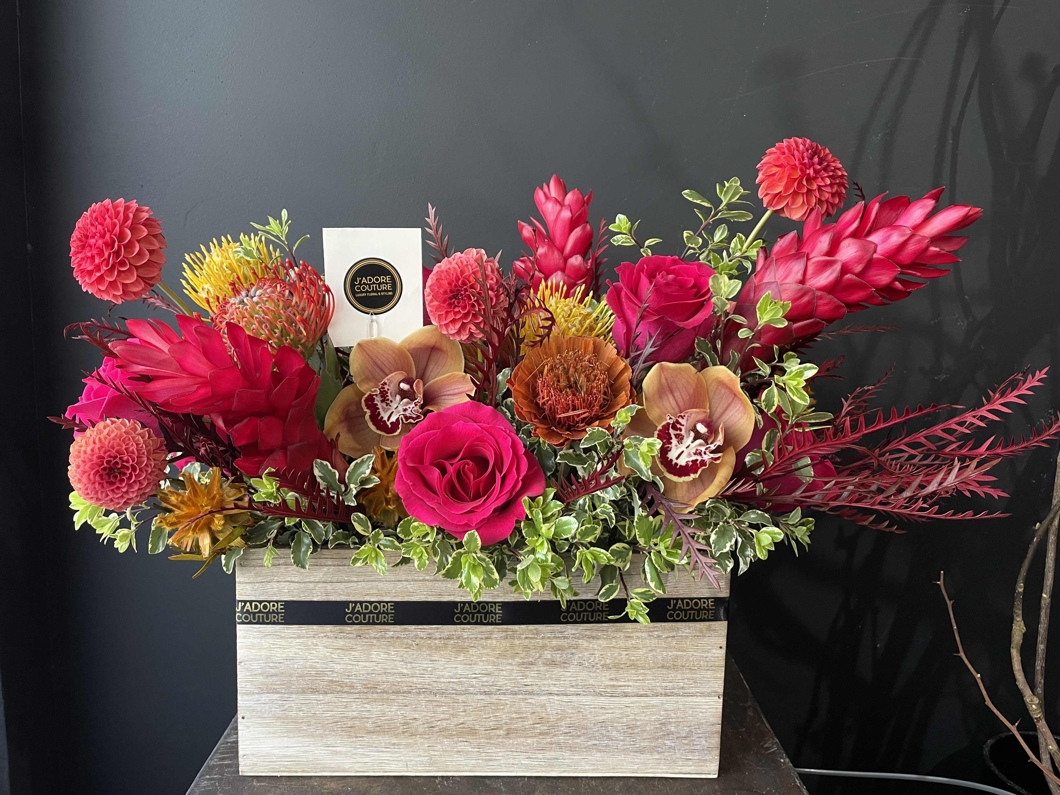 Bright mixed floral arrangement in a wooden box with a perfume bottle card