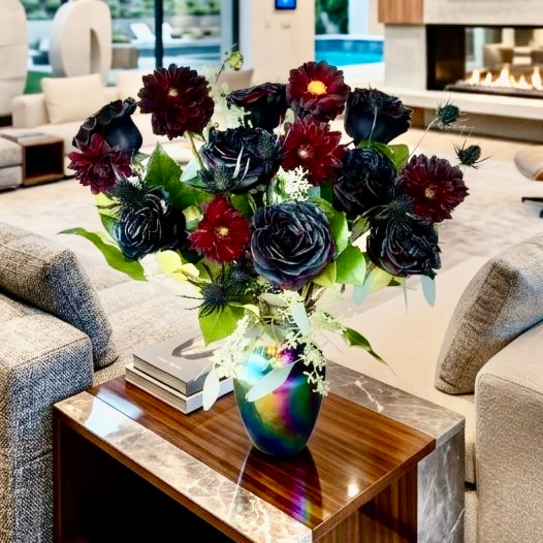 Dark floral arrangement in a rainbow vase on a coffee table