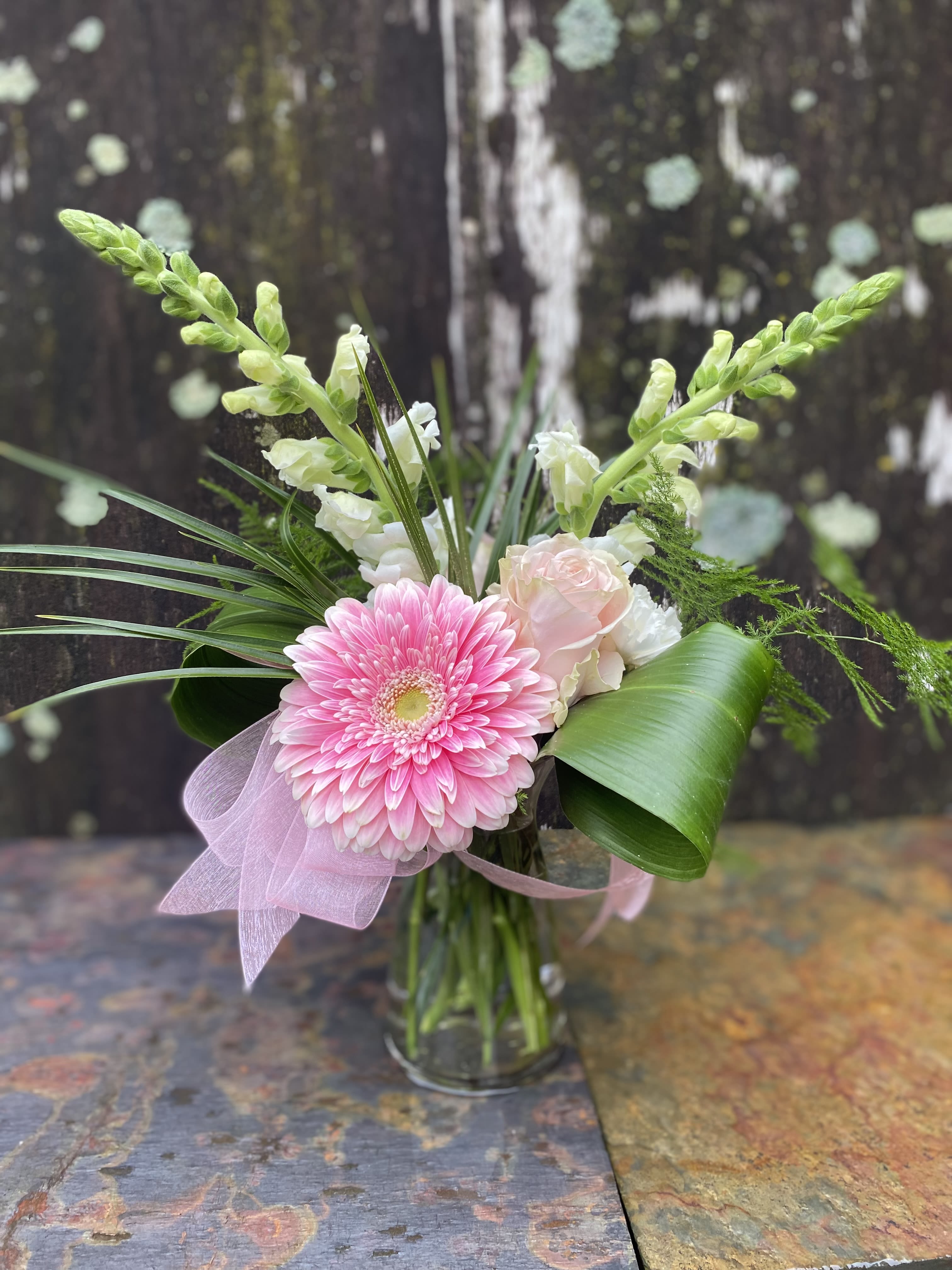 Pink gerbera bouquet in a glass vase with white blooms and ribbon
