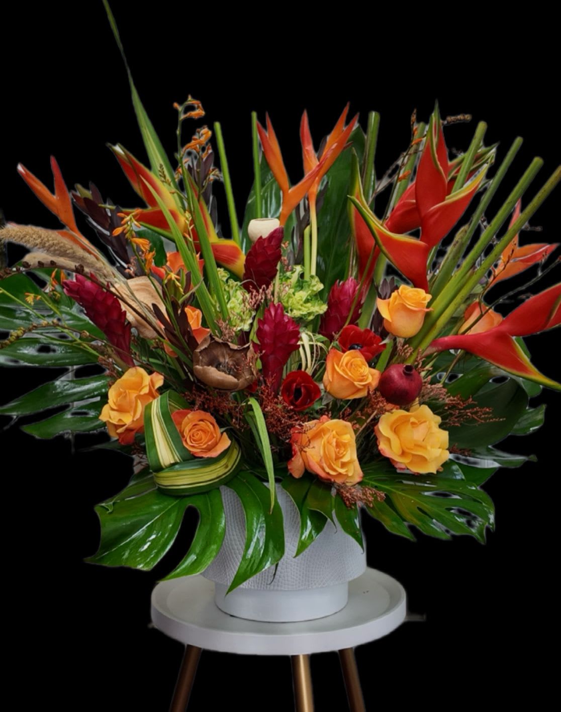 Tropical floral arrangement with orange roses and red heliconia in a white vase