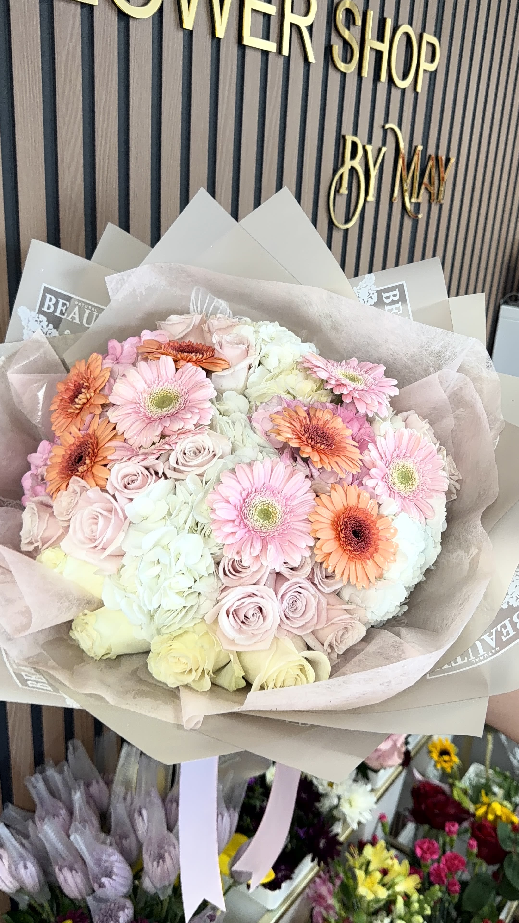 Gerberas Isle  - Soft, romantic pastels take center stage in this gerbera-and-hydrangea hand-tied bouquet-perfect as a birthday bouquet, Mother's Day arrangement, or a thoughtful anniversary gift. Gerbera daisies in pale yellow and peach mingle with full white and blush hydrangea clusters and delicate pink/blush roses to create an airy, gently rounded silhouette that reads as both celebratory and tender. The look is made for the person you want to make feel seen and cherished.  Tightly gathered and wrapped in layered cream, beige, and translucent decorative paper, the arrangement is finished with a sheer ribbon tail for a polished, gift-ready presentation. Textures contrast beautifully: the plush, cloud-like hydrangeas, the smooth petals of roses, and the cheerful faces of gerberas combine for visual depth and a soft fragrance. Sized as a generous hand-tied bouquet, it's an easy-to-hold statement that arrives ready to display or pass on.  Lovely for birthdays, thank-you gestures, spring celebrations, and anniversary moments, this bouquet reads as both everyday sweetness and special-occasion beauty-she'll feel genuinely celebrated. For best enjoyment, keep stems in fresh water, away from direct heat or draft, and refresh the water every couple of days to extend vase life.