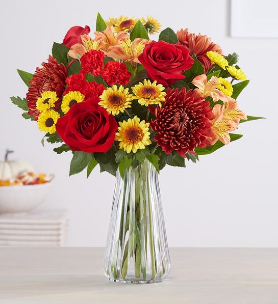 Autumn Charm  - A landscape alive with color. Our new bouquet celebrates fall’s magic in radiant style. A mix of red and orange blooms with warm hints of copper and bronze, Bouquet made with  red roses and mini carnations, yellow Viking mum, bronze cremones, copper button poms and orange Peruvian lilies (alstroemeria) 