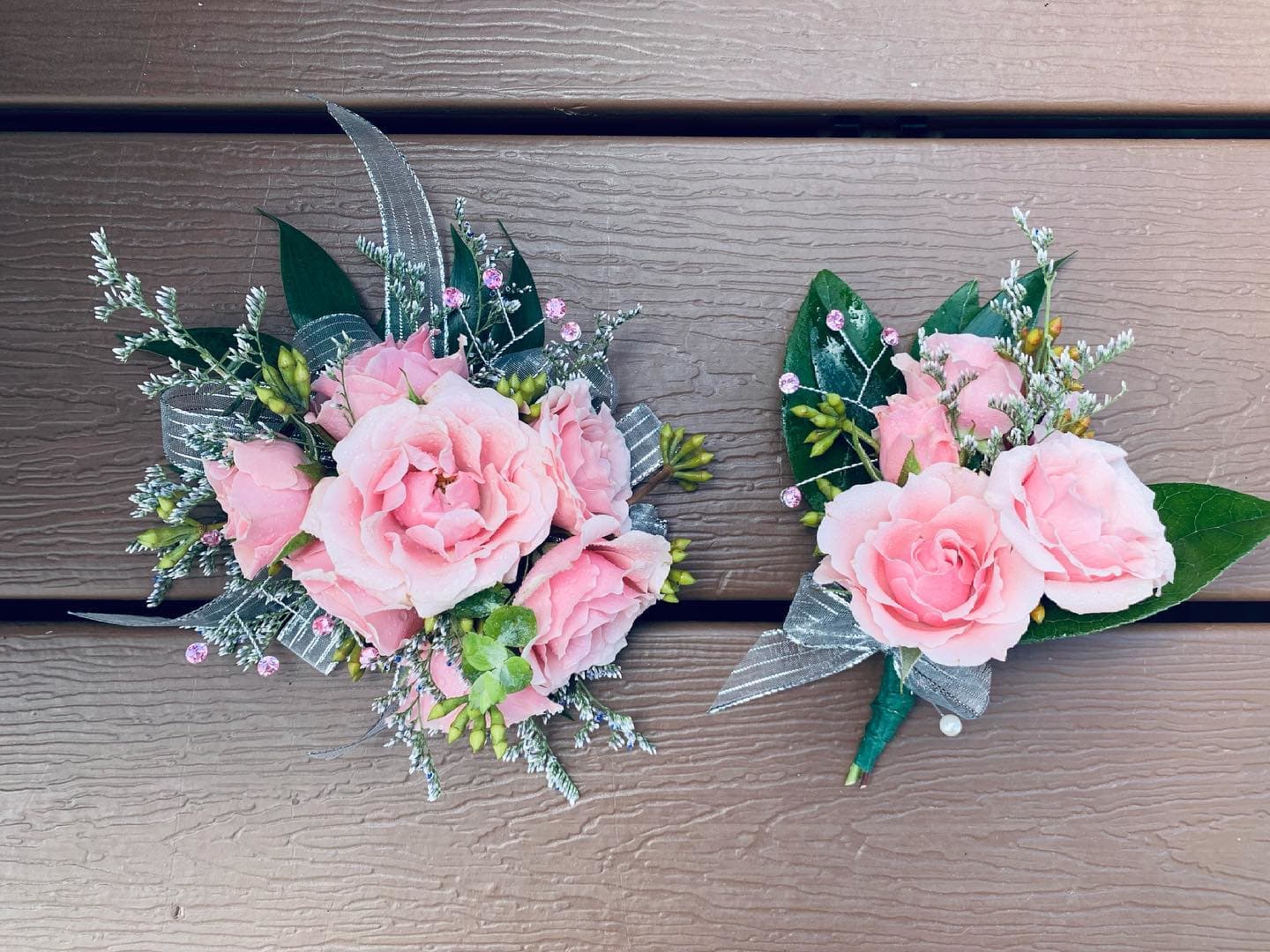 Two pink rose boutonnieres with silver ribbon and greenery