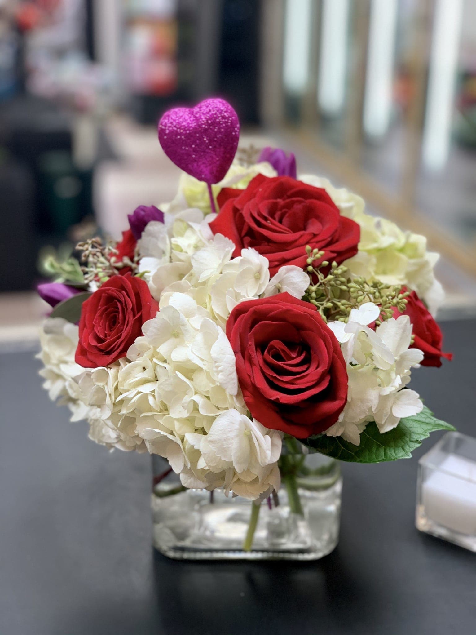 Red roses and white hydrangeas in a glass vase with a pink heart pick