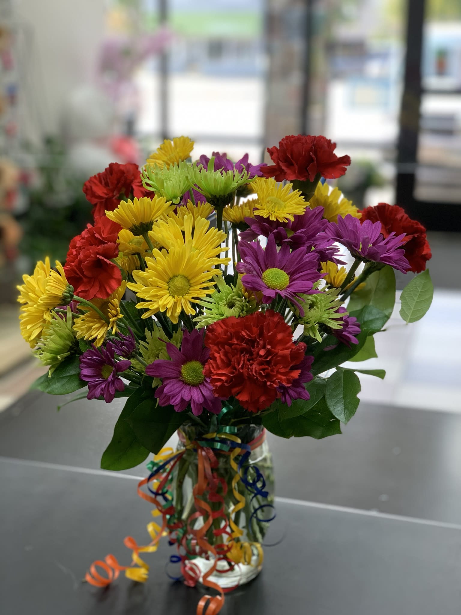 Colorful bouquet of daisies and carnations in a glass vase with ribbon curls