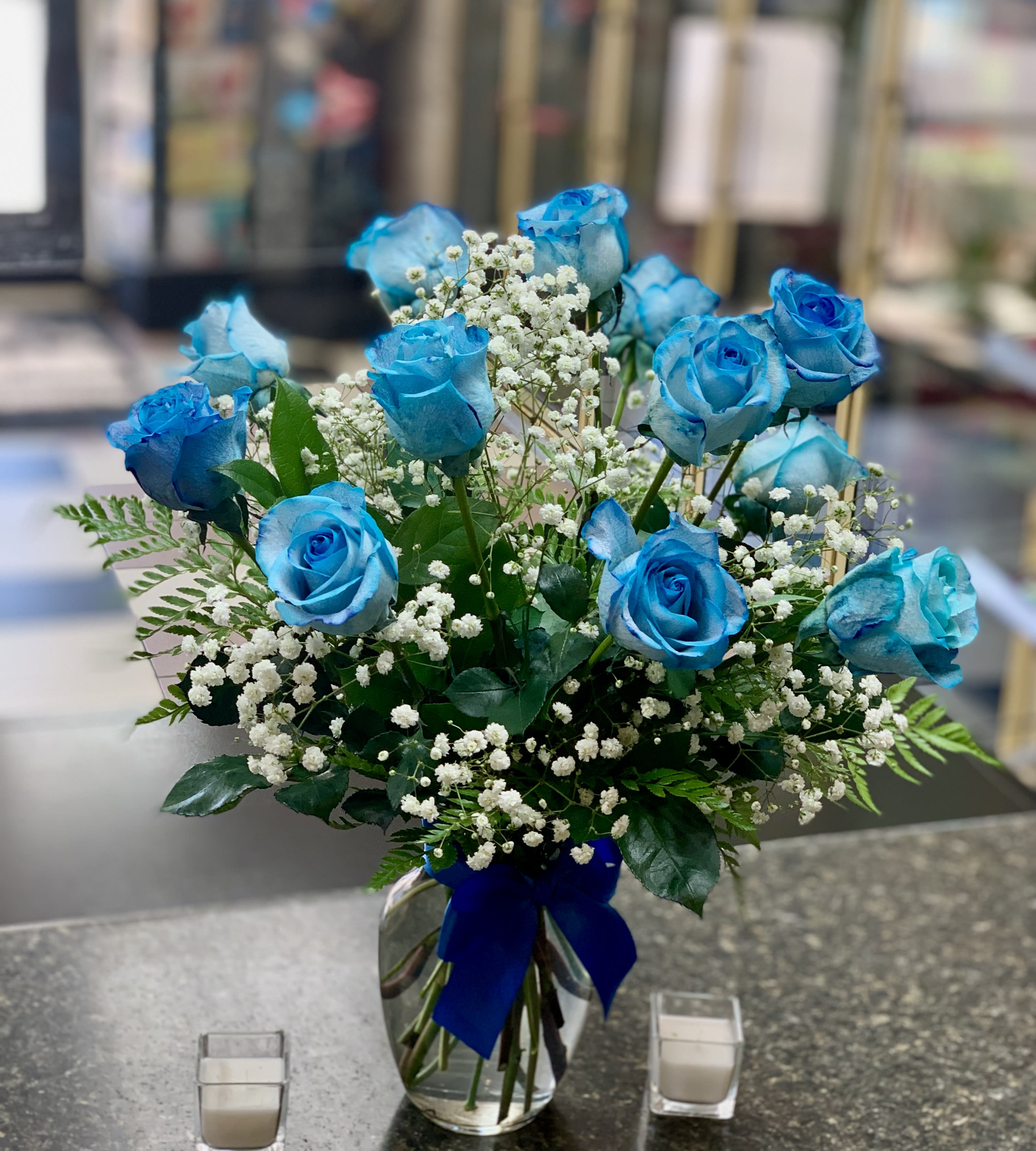 Blue roses in a glass vase with baby's breath and a blue ribbon