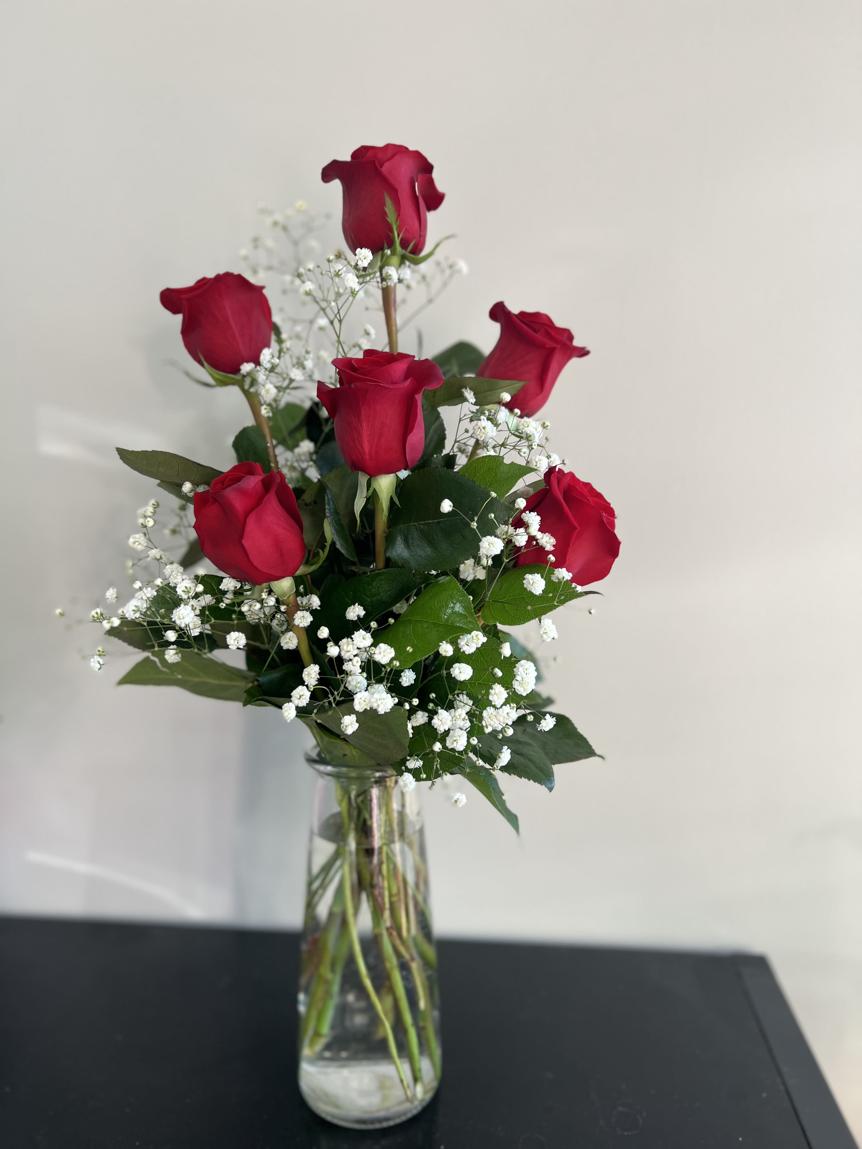 Red roses arranged in a clear glass vase with white baby's breath