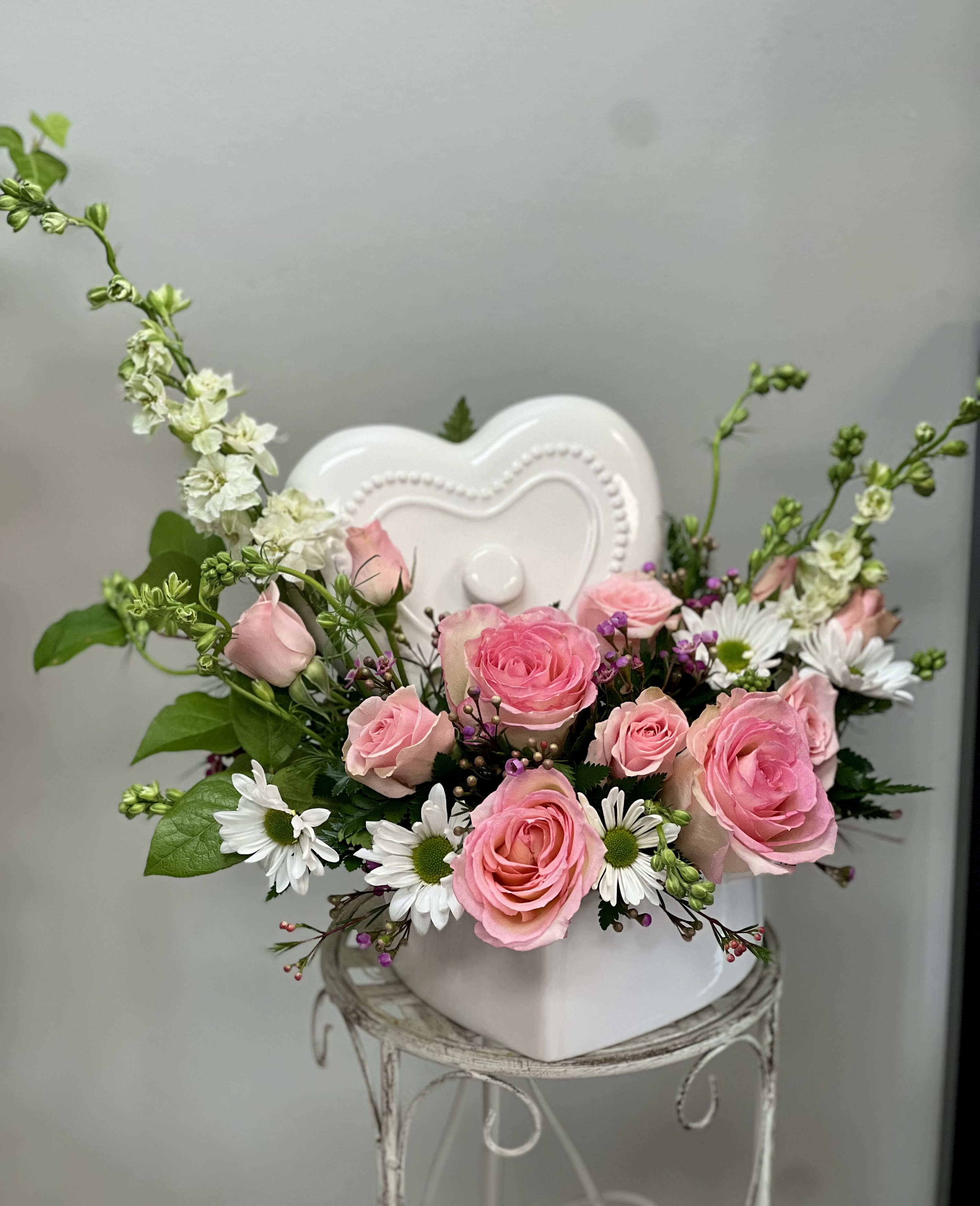 Pink roses and white daisies arranged in a white heart-shaped vase