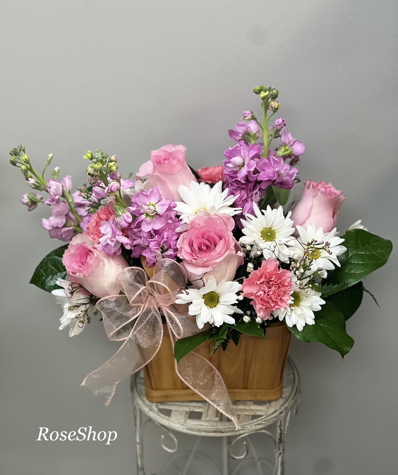 Blush Garden Delight  - A charming blend of soft pink roses, cheerful daisies, delicate carnations, and fragrant stock blooms—artfully arranged in a rustic wooden basket. This design brings a fresh, garden‑inspired feel to any space.  Perfect for birthdays, thank‑yous, or simply brightening someone’s day, it’s one of our most-loved arrangements for its sweetness, versatility, and timeless beauty. 