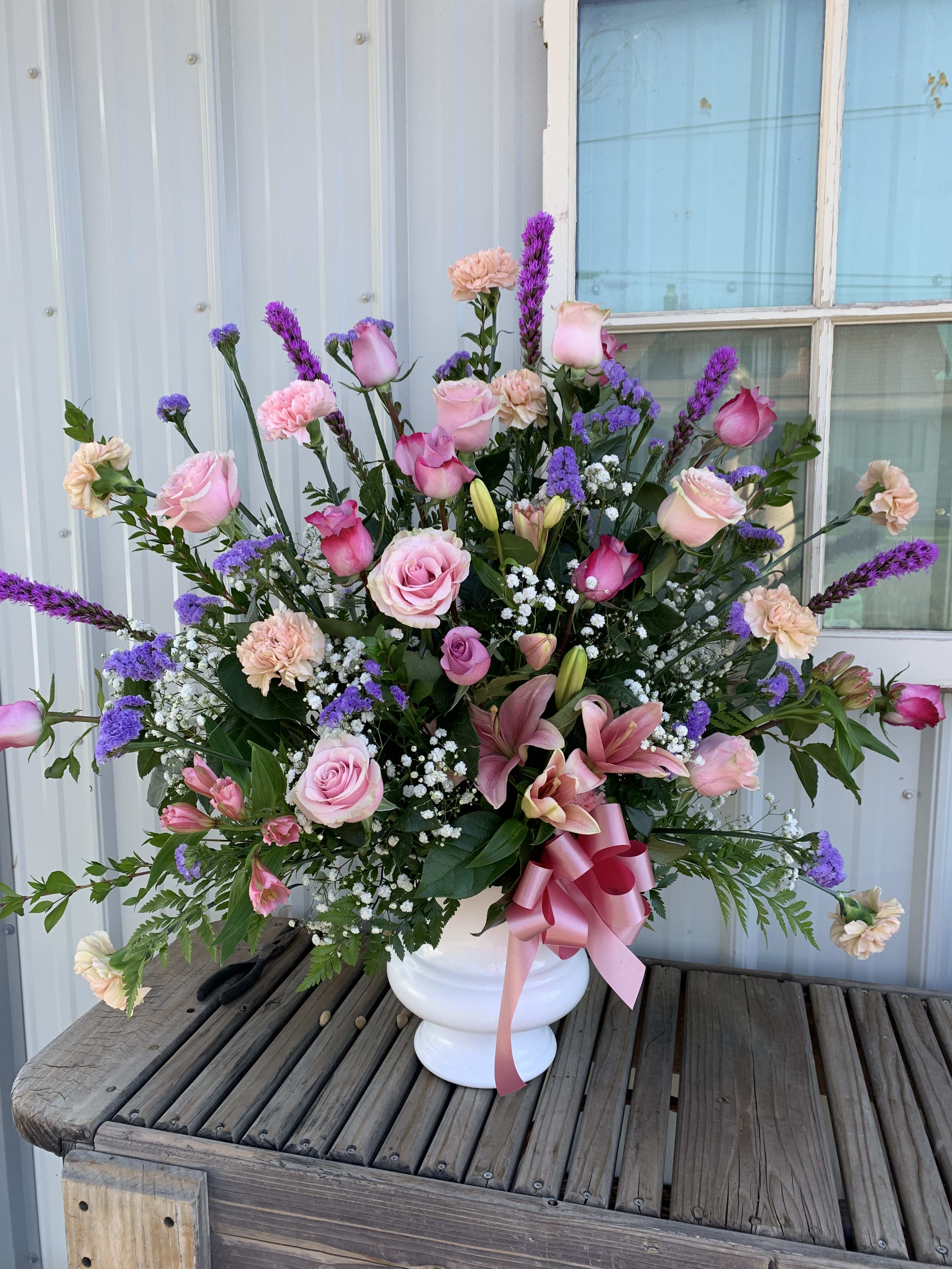 Pink and purple mixed flower arrangement in a white vase with a ribbon