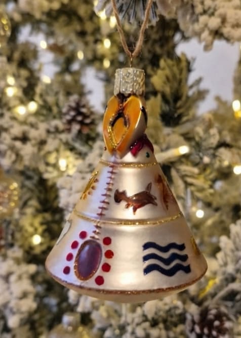 Decorative bell-shaped Christmas ornament hanging in front of a lit tree