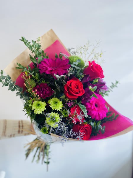 Hand-tied bouquet of red roses, bright pink gerberas and green mums wrapped in kraft and pink paper