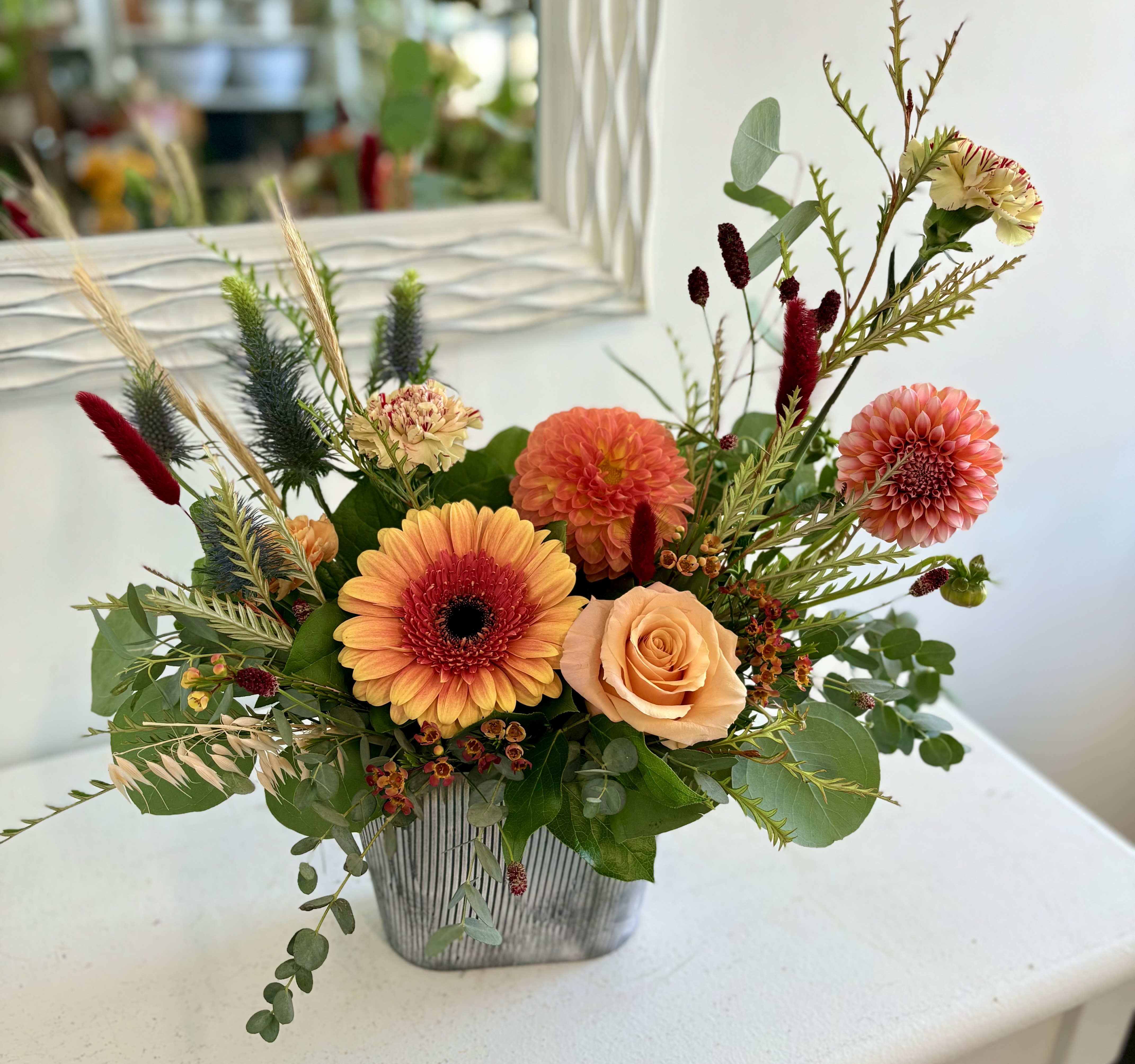 Low orange and peach flower arrangement with gerbera daisy, dahlias, and roses in a gray rectangular vase