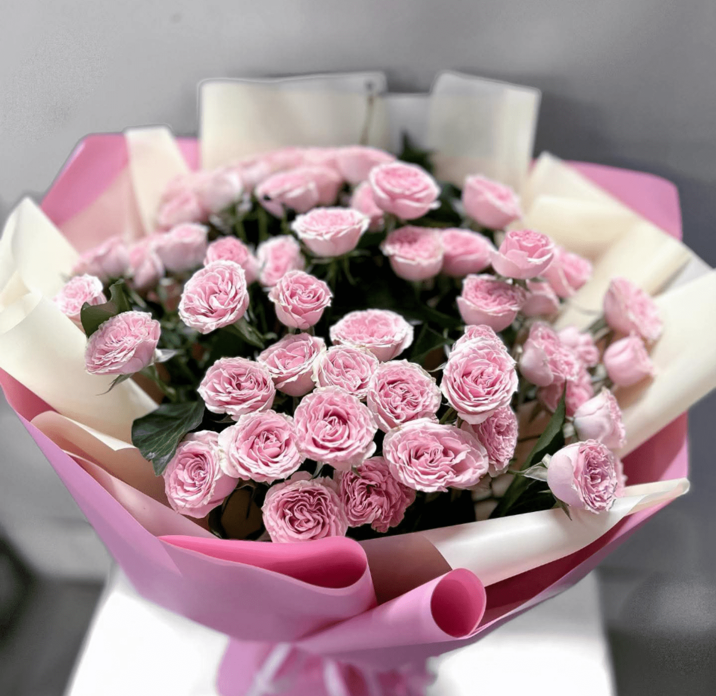 Mini Bella Spray Roses Bouquet - Pink and White Spray Roses - A dense cluster of soft pink spray roses makes a quietly romantic birthday bouquet or anniversary gift that feels both intimate and celebratory. The Mini Bella flower arrangement is a rounded, hand-tied spray rose bouquet crafted for moments when you want the person you're thinking of to feel truly seen-whether you're marking a birthday, saying happy anniversary, or sending a sweet Valentine's Day surprise.  Tightly packed blush-to-medium pink spray roses create a full, textured dome of layered petals, accented by hints of fresh green foliage. The stems are finished in layered pink and cream decorative wrap and tied with a neat ribbon for a polished, feminine presentation that arrives ready to set on a bedside table or desk. Compact and elegant, Mini Bella is ideal for expressing affection in a way that's both understated and deeply felt; order with standard care instructions to keep blooms hydrated and away from direct heat for the best vase life.