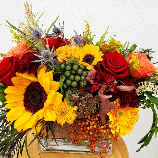 Bright mixed bouquet with sunflowers, red roses, and orange blooms in a clear vase