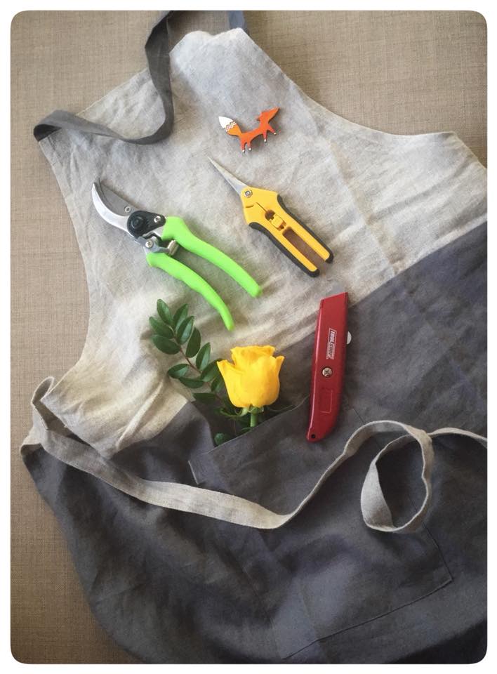 Floral apron with pruning shears, a yellow rose, and a small fox pin