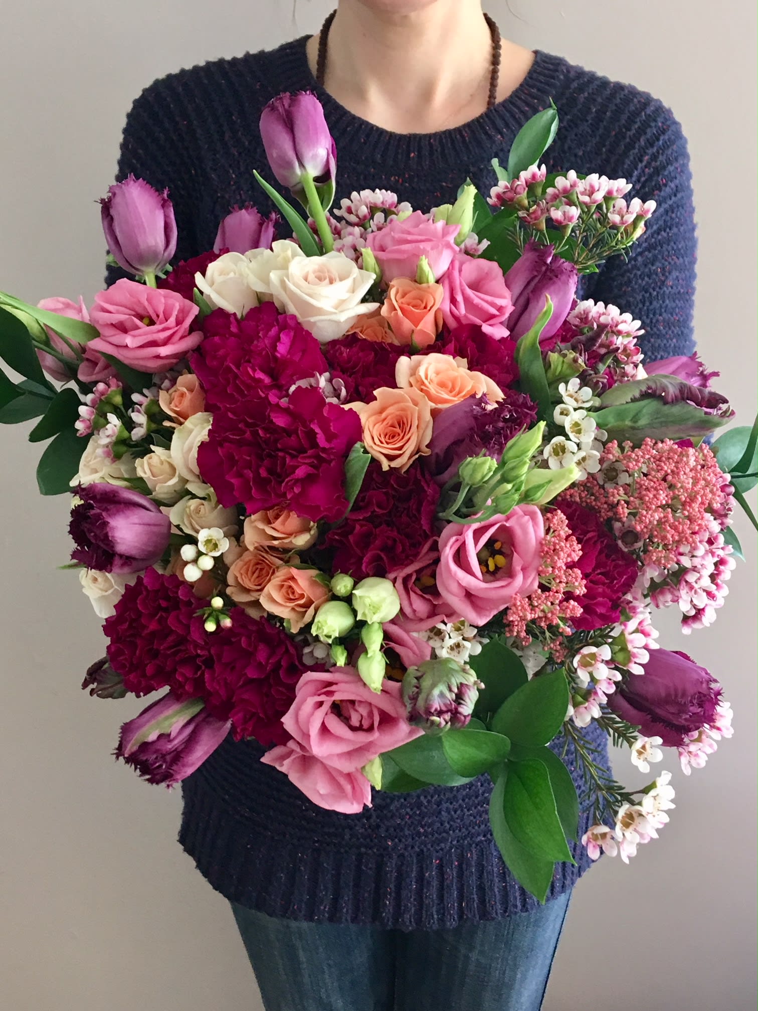 Large bouquet of pink, purple, and peach flowers held by a person