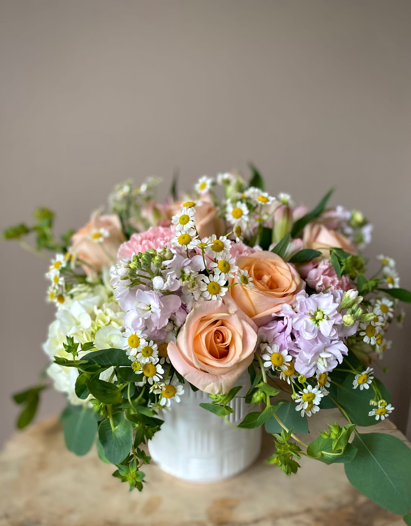 Peach roses and pastel flowers arranged in a white vase