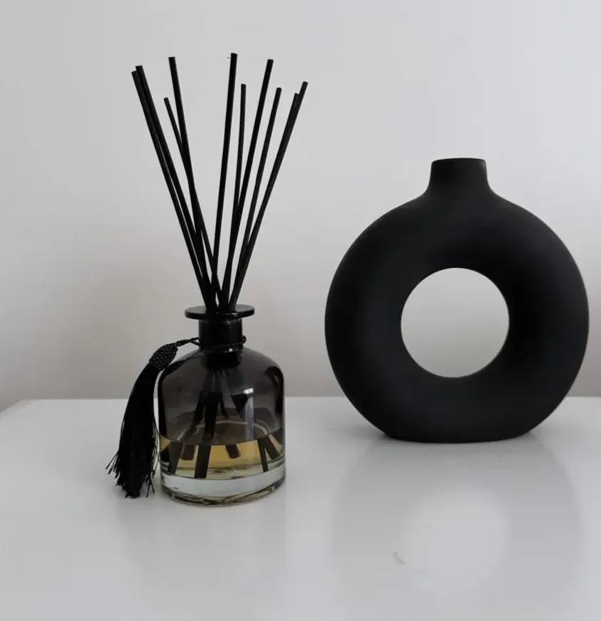 Black reed diffuser bottle with a round black vase beside it