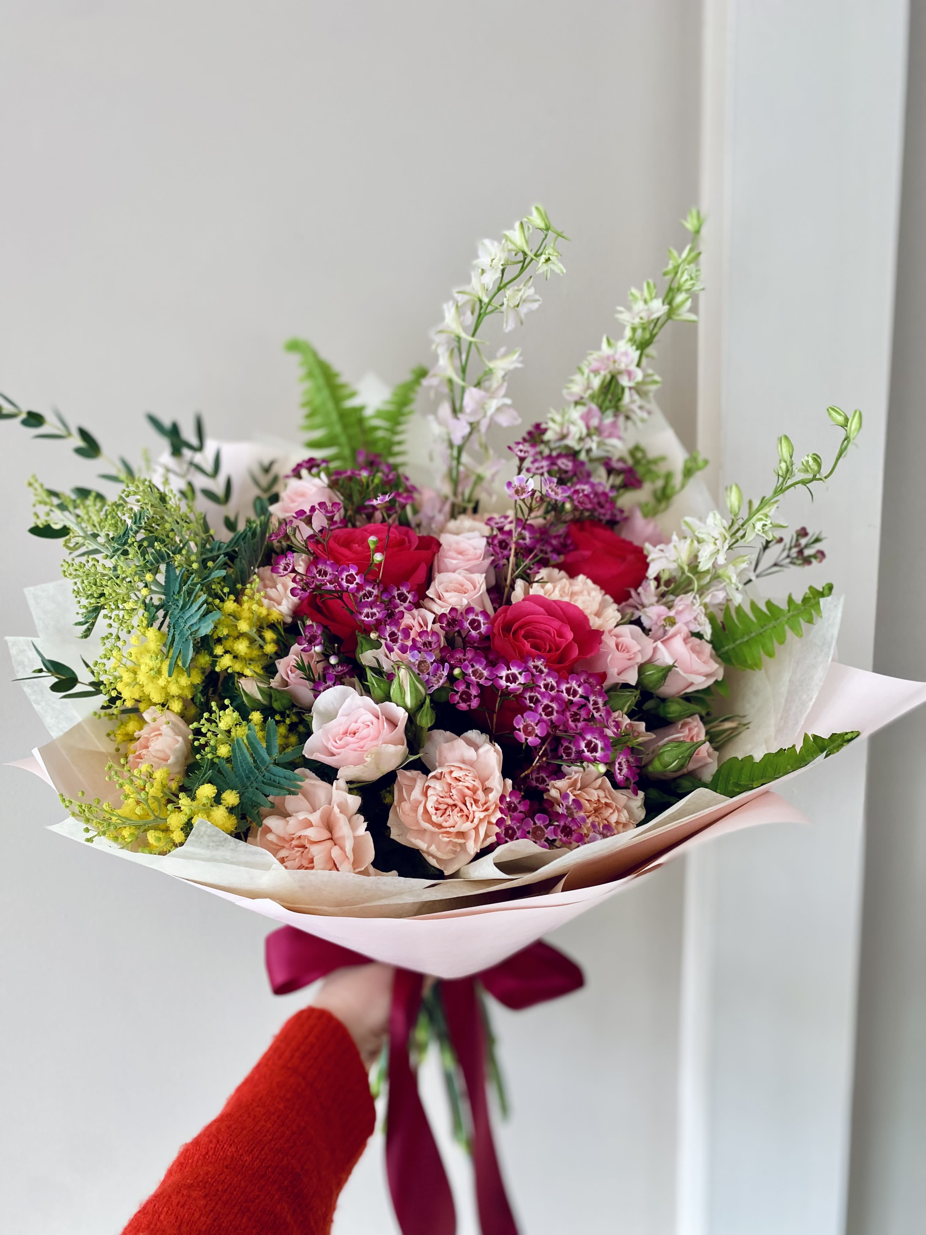 Hand-tied bouquet of pink and red roses with purple accents