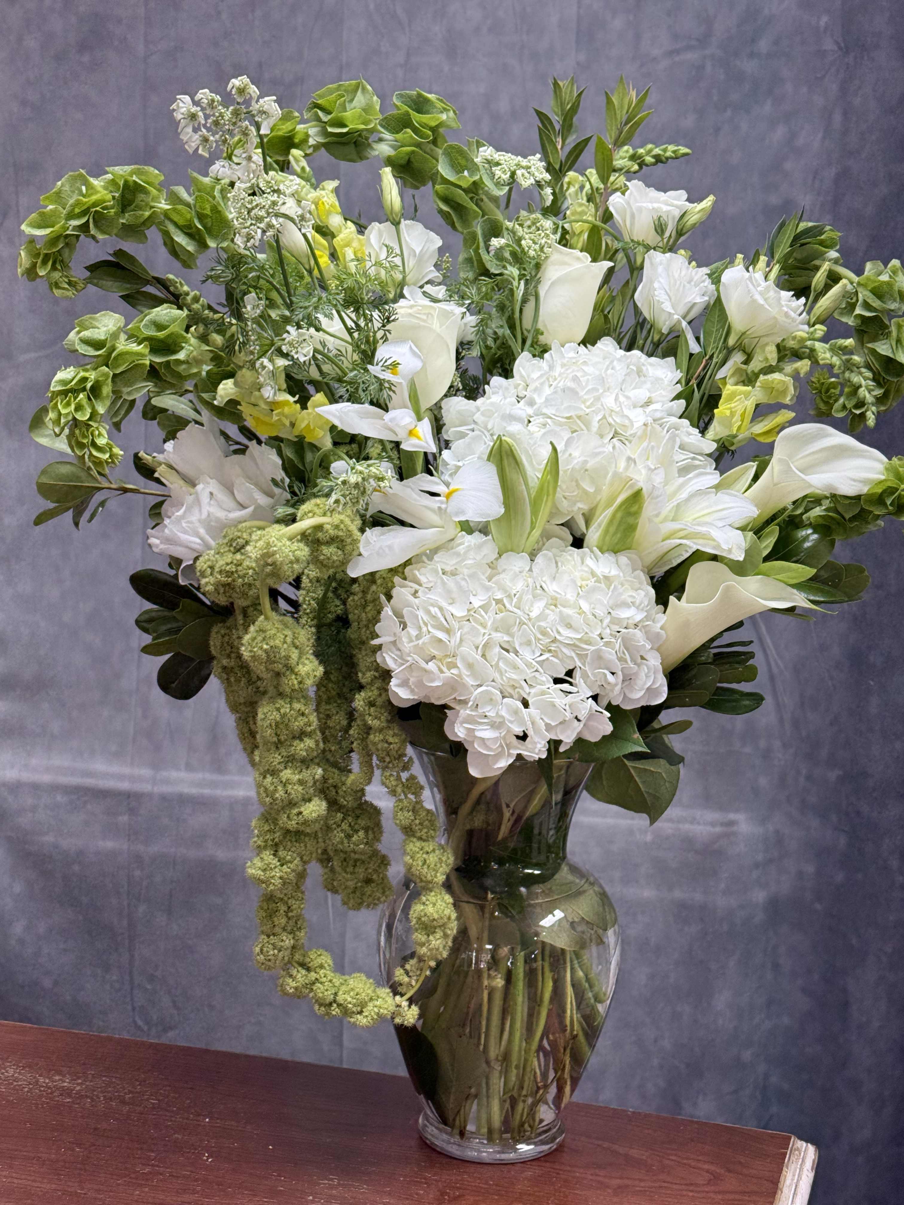 White flowers and green accents arranged in a clear glass vase