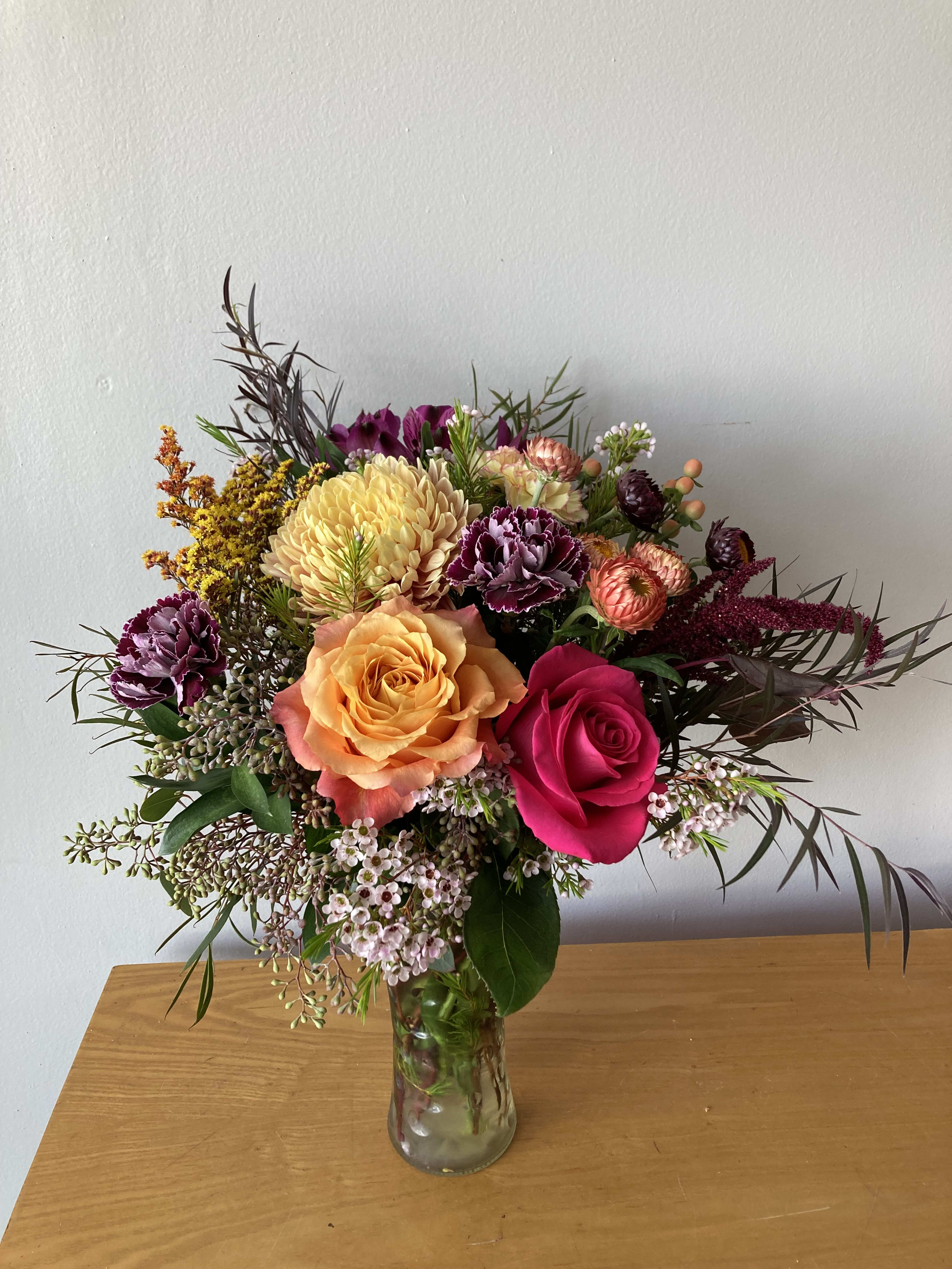 Mixed bouquet of roses, chrysanthemums, and small filler flowers in a glass vase
